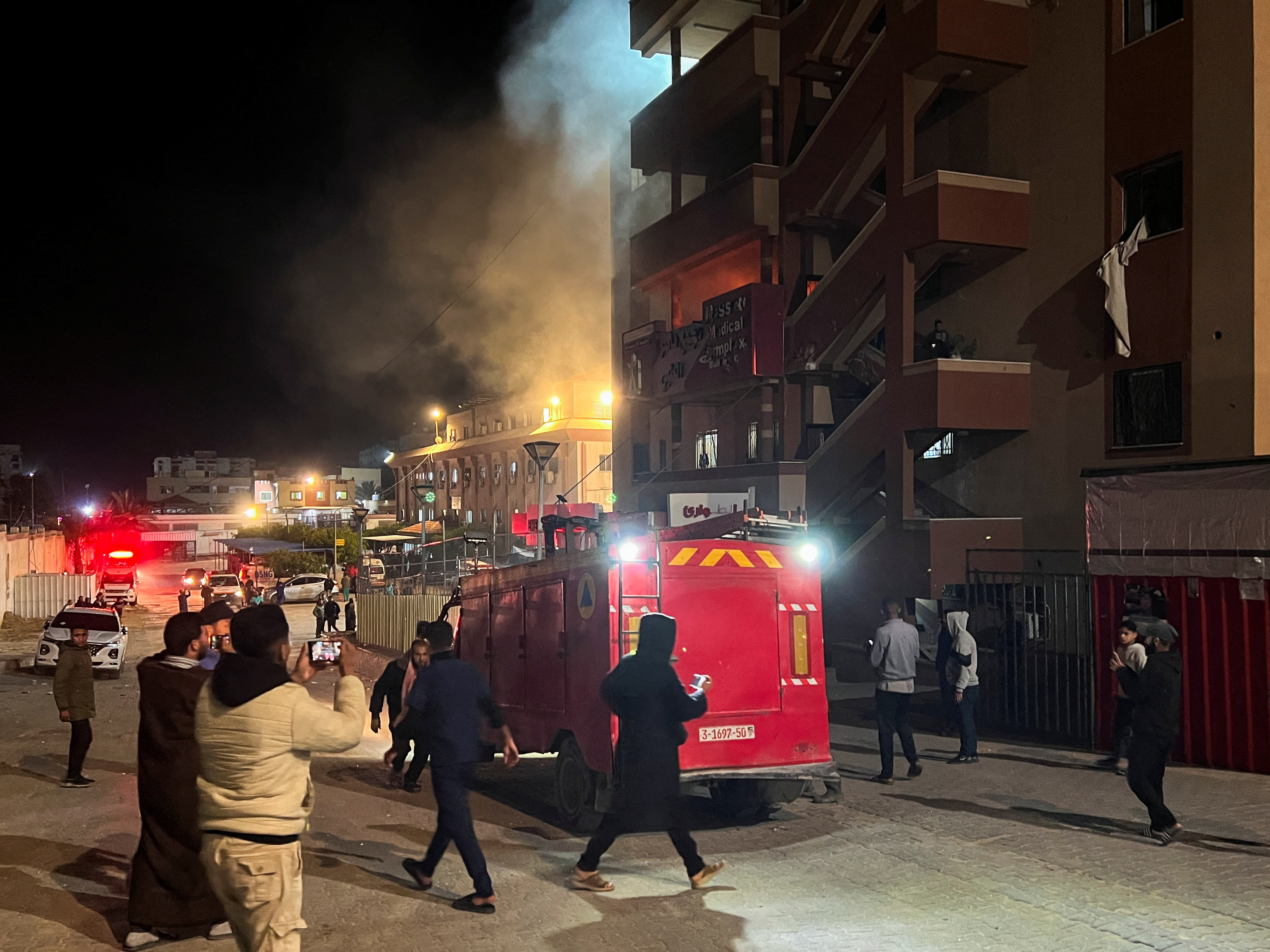 Smoke rises after an Israeli raid on Nasser Hospital as an ambulance and people rush around.
