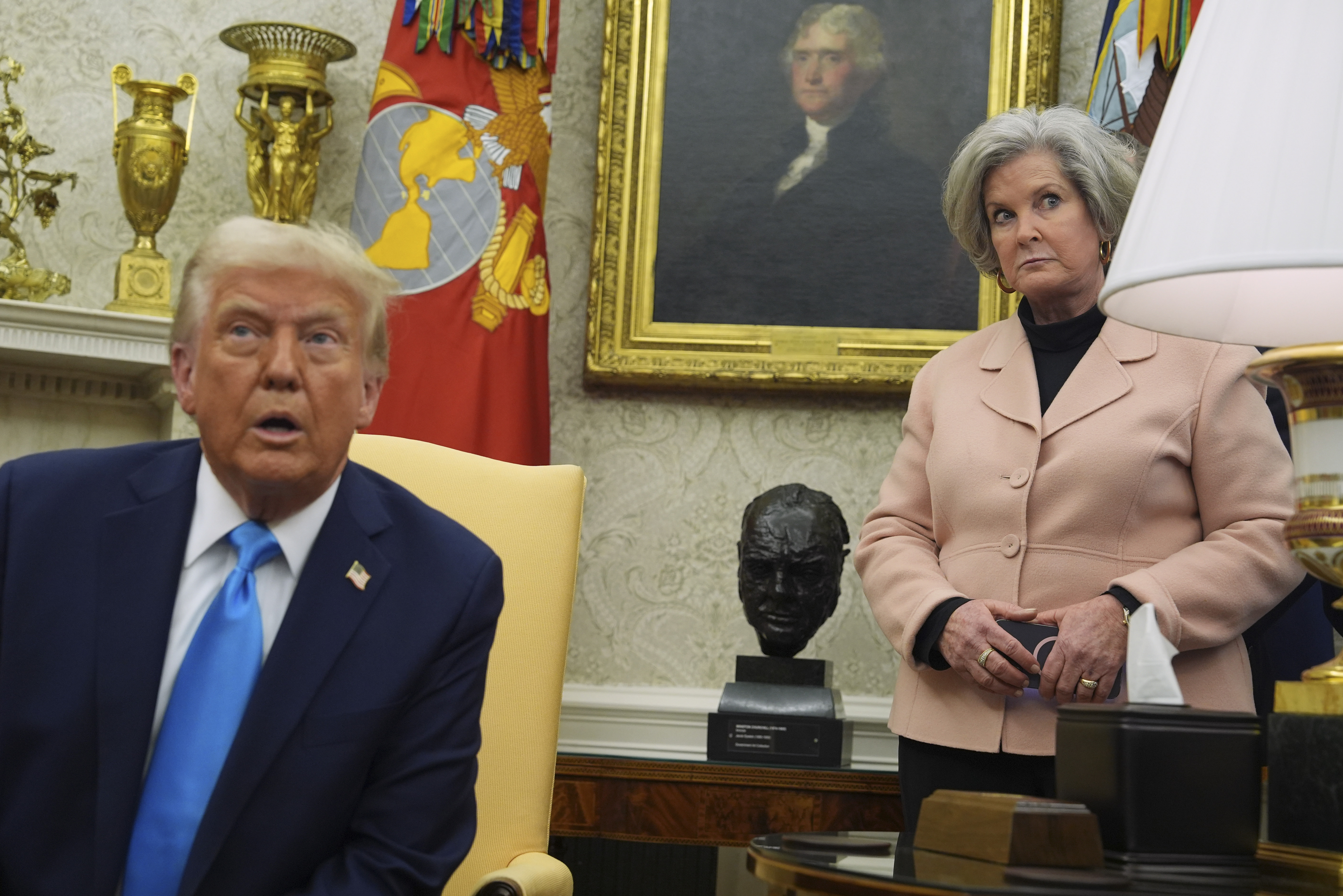 Susie Wiles stands behind a seated Donald Trump in the Oval Office.