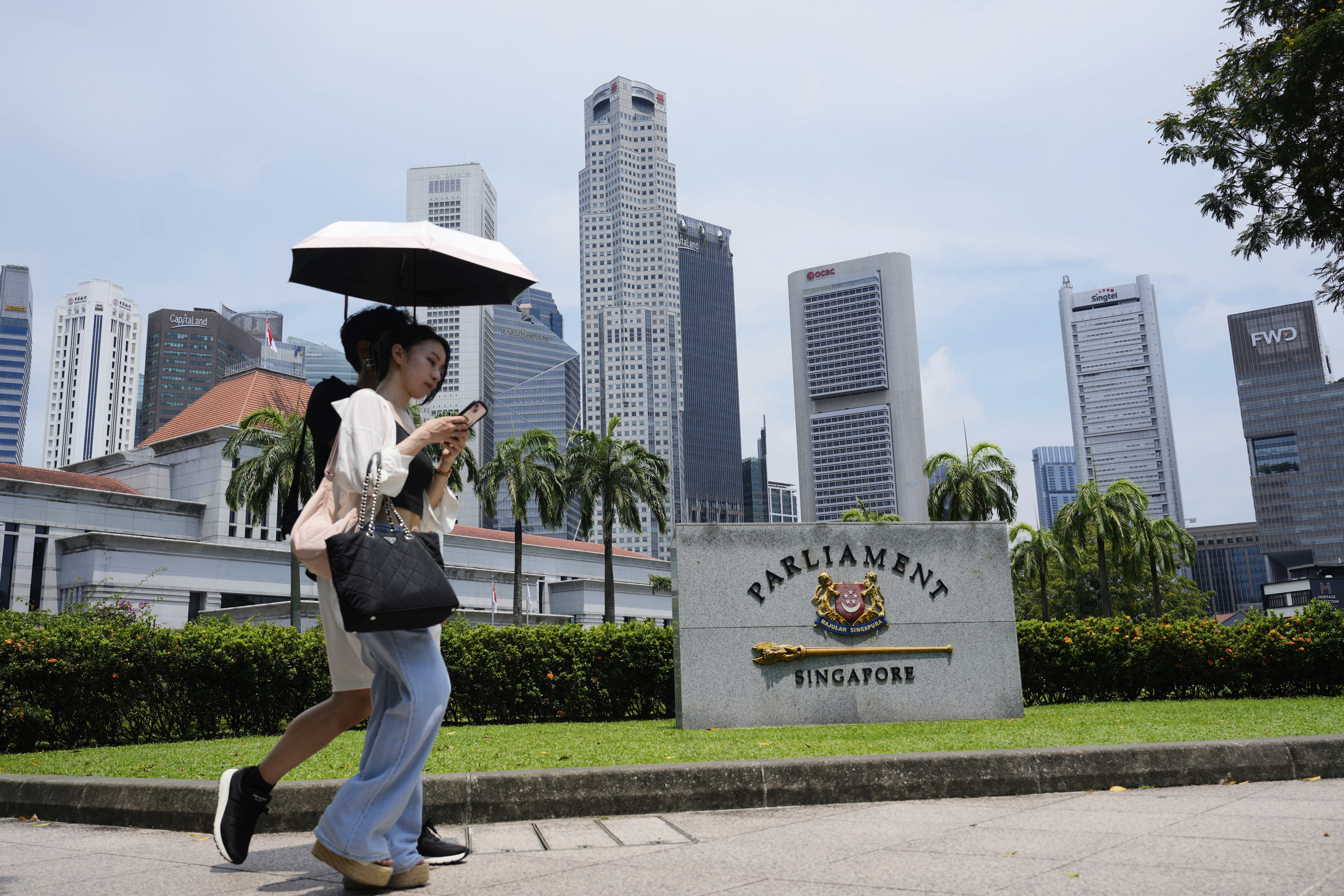 Pedestrians shield from the sun with an umbrella as they walk in front of the parliament building in Singapore in May 2025