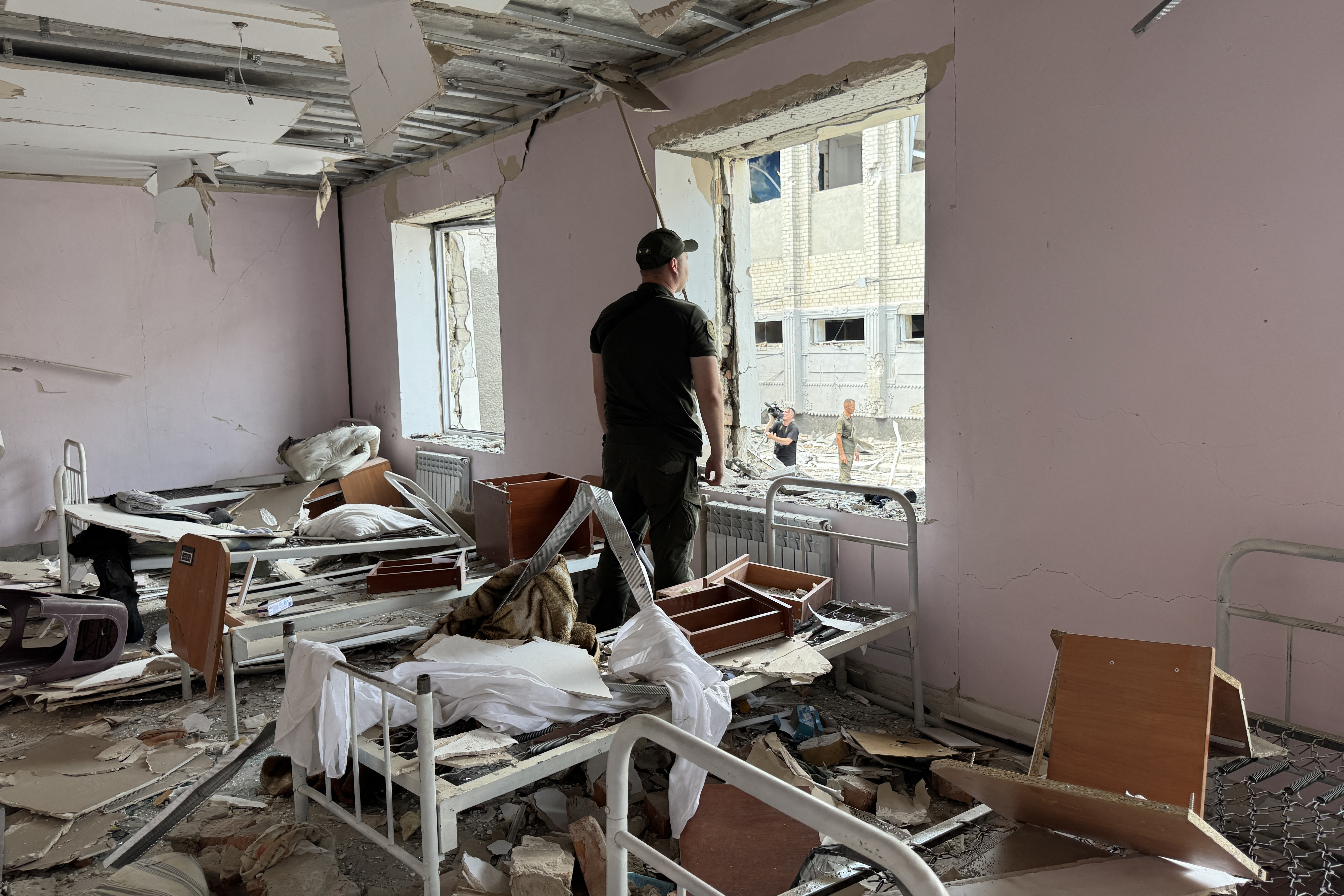 A man looks out of a window in a damaged room.