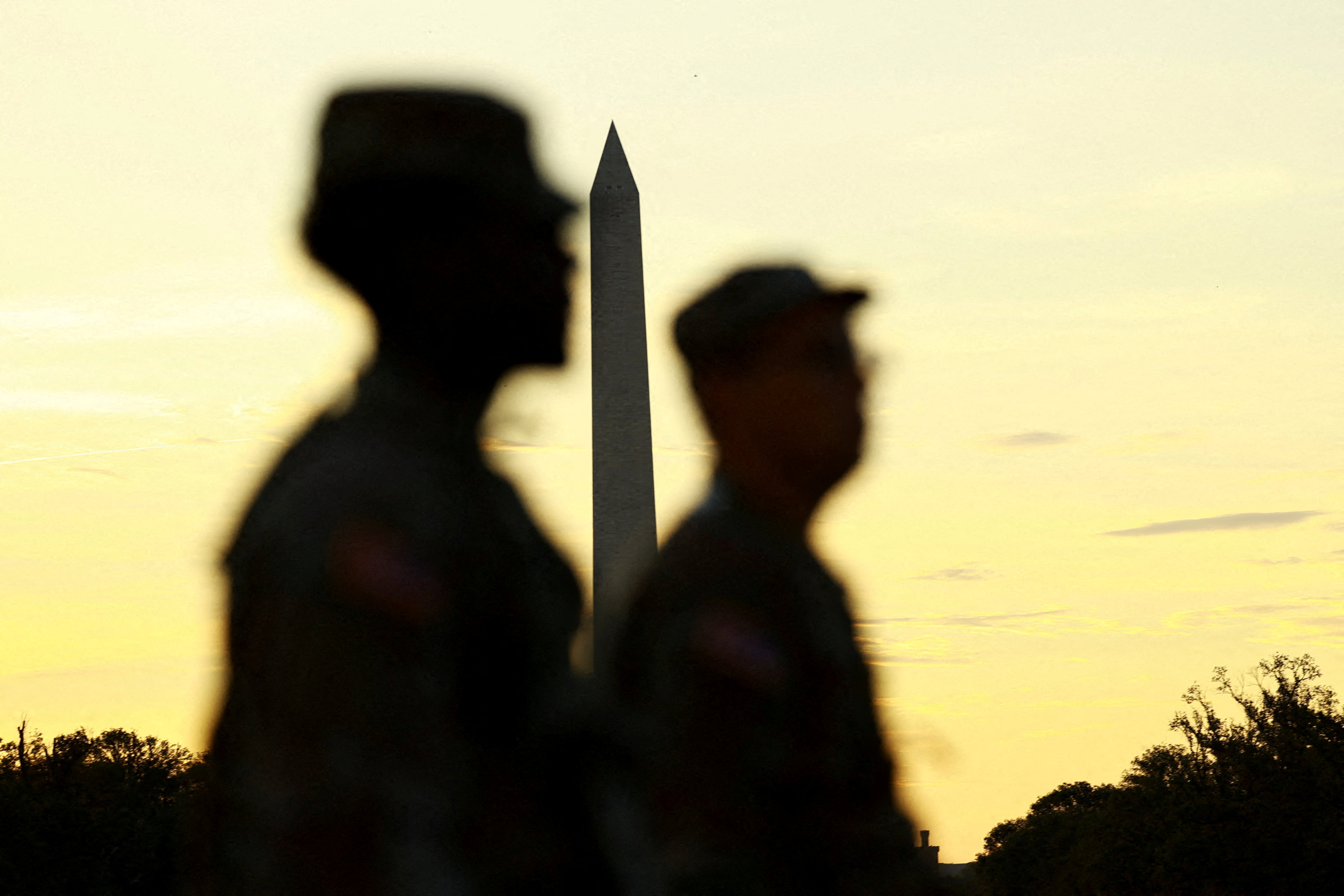 Troops stand in silhouette in front of Washington monument
