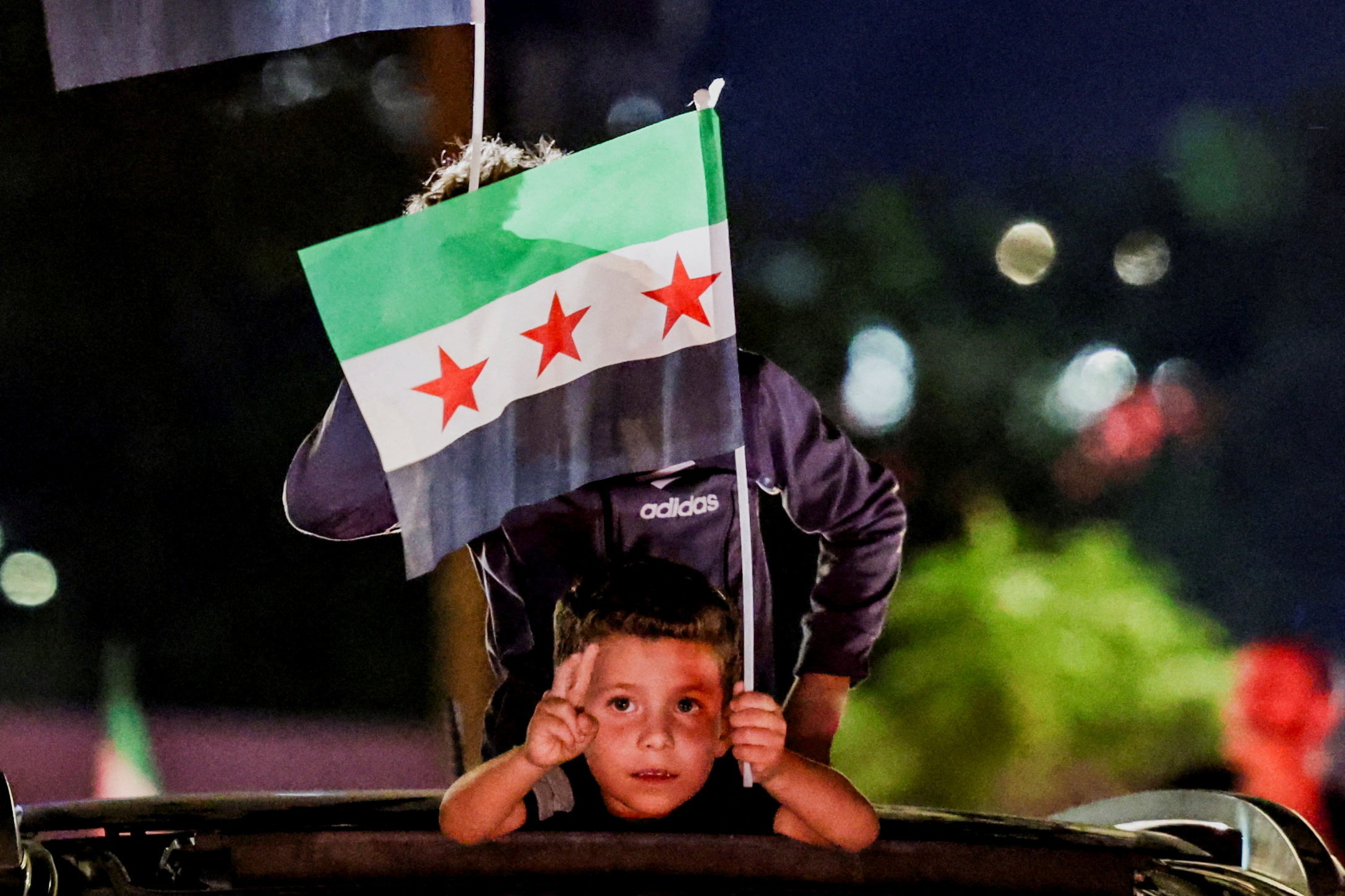 A child waves a Syrian flag while watching a nighttime broadcast from the UNGA
