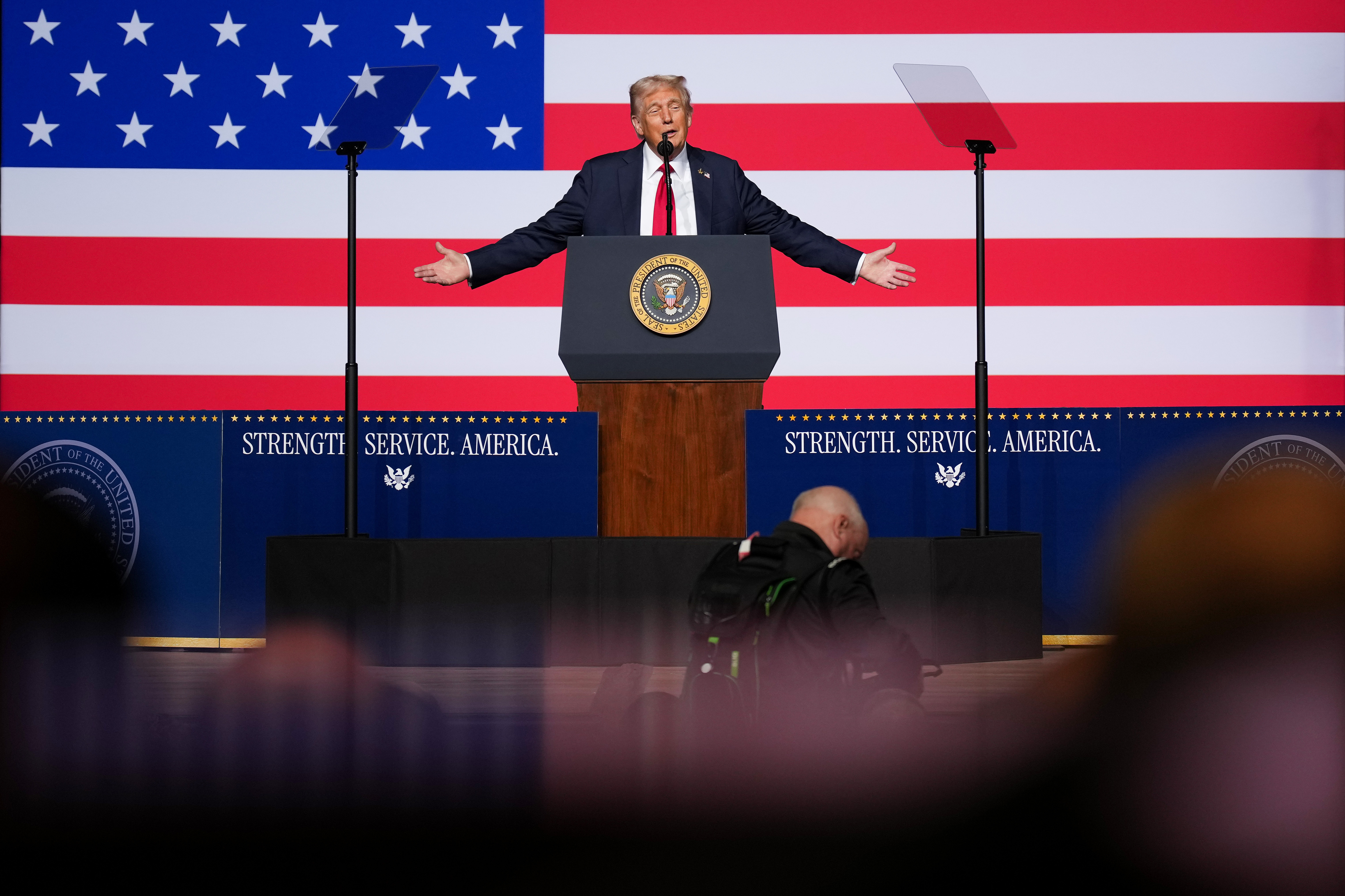 Trump at a podium in front of a US flag speaks to top military leaders.