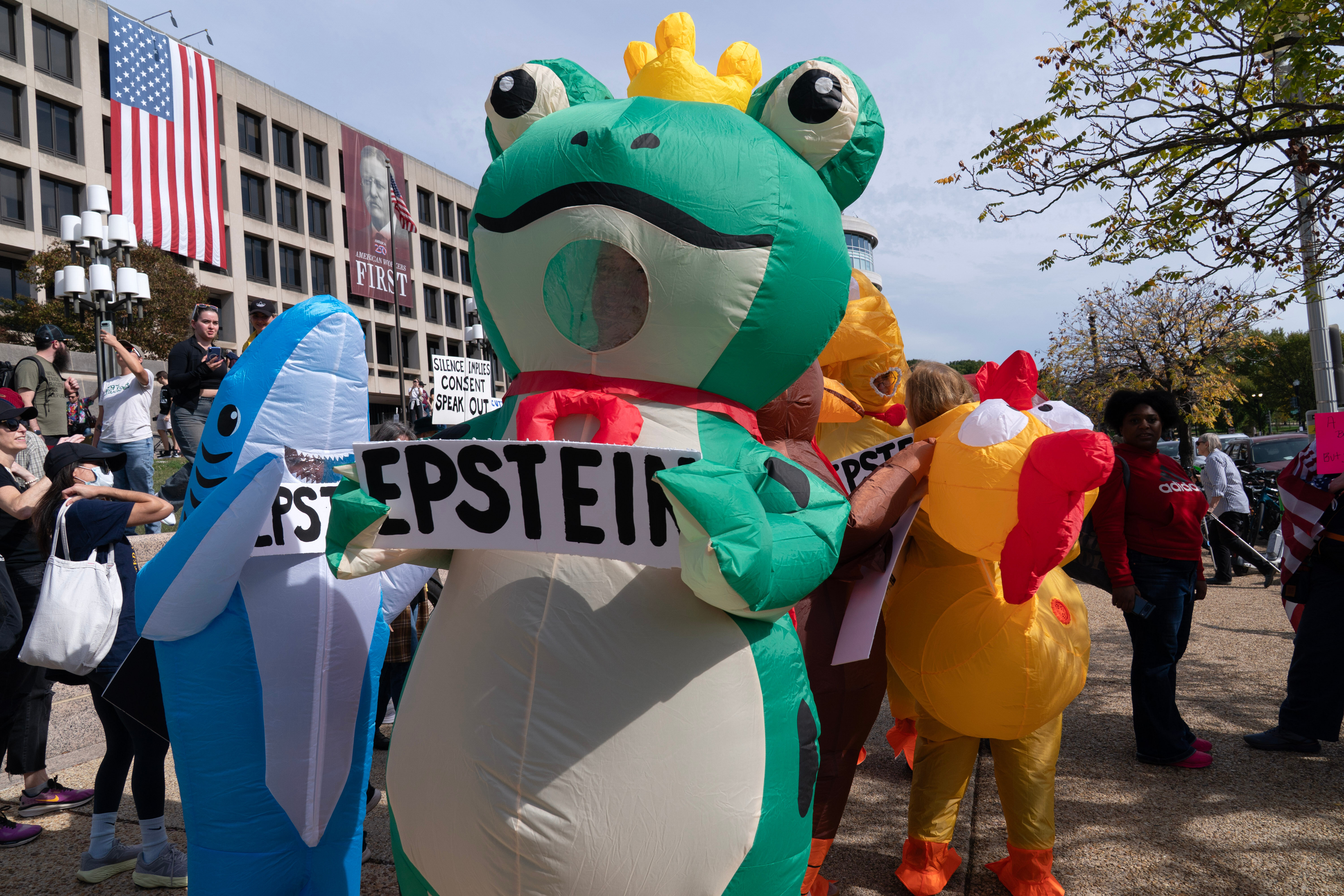 A person in an inflatable frog costume marches with a sign that reads, "Epstein."