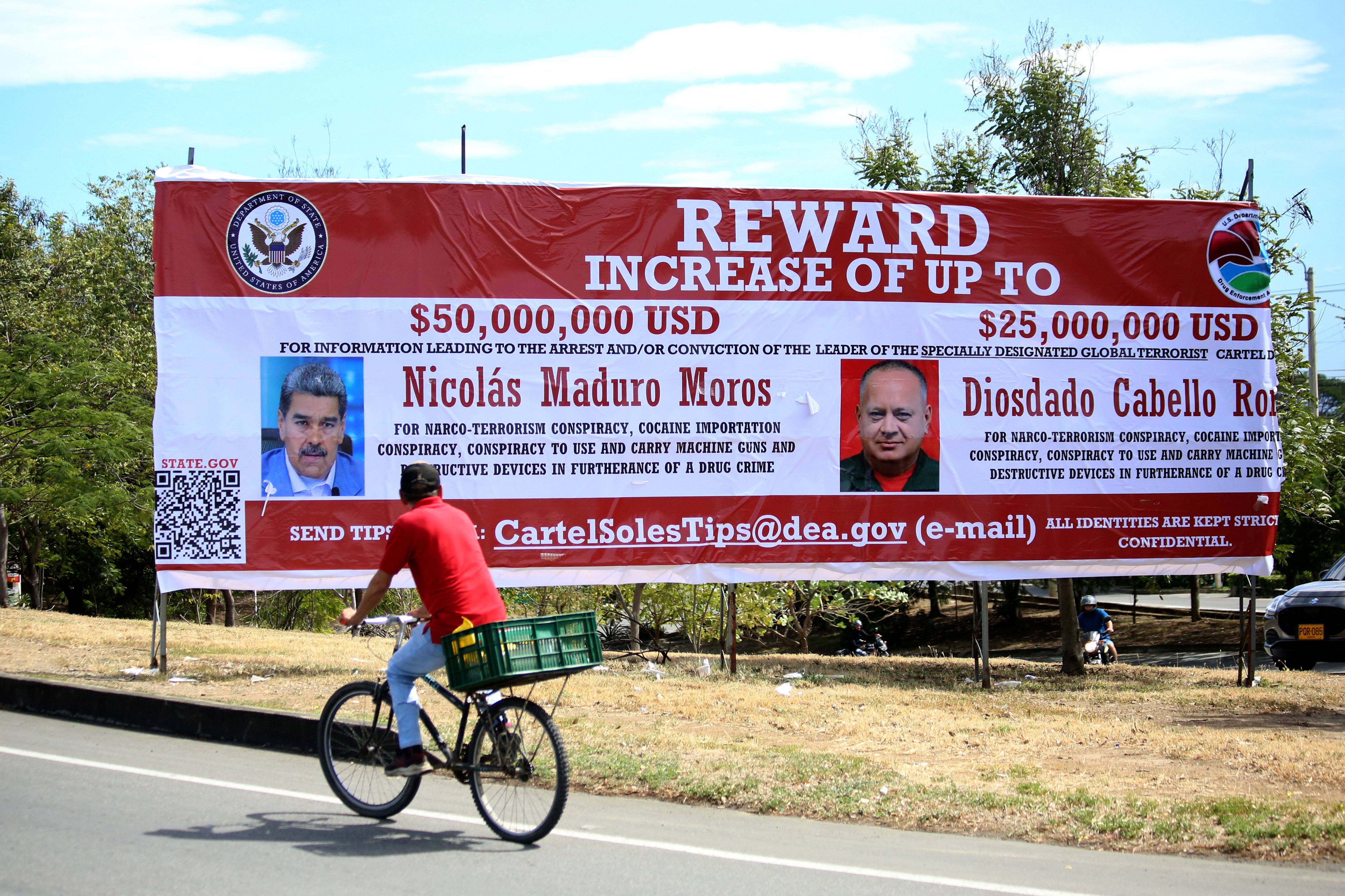 A man bicycles past a billboard in Colombia advertising the reward against Maduro.