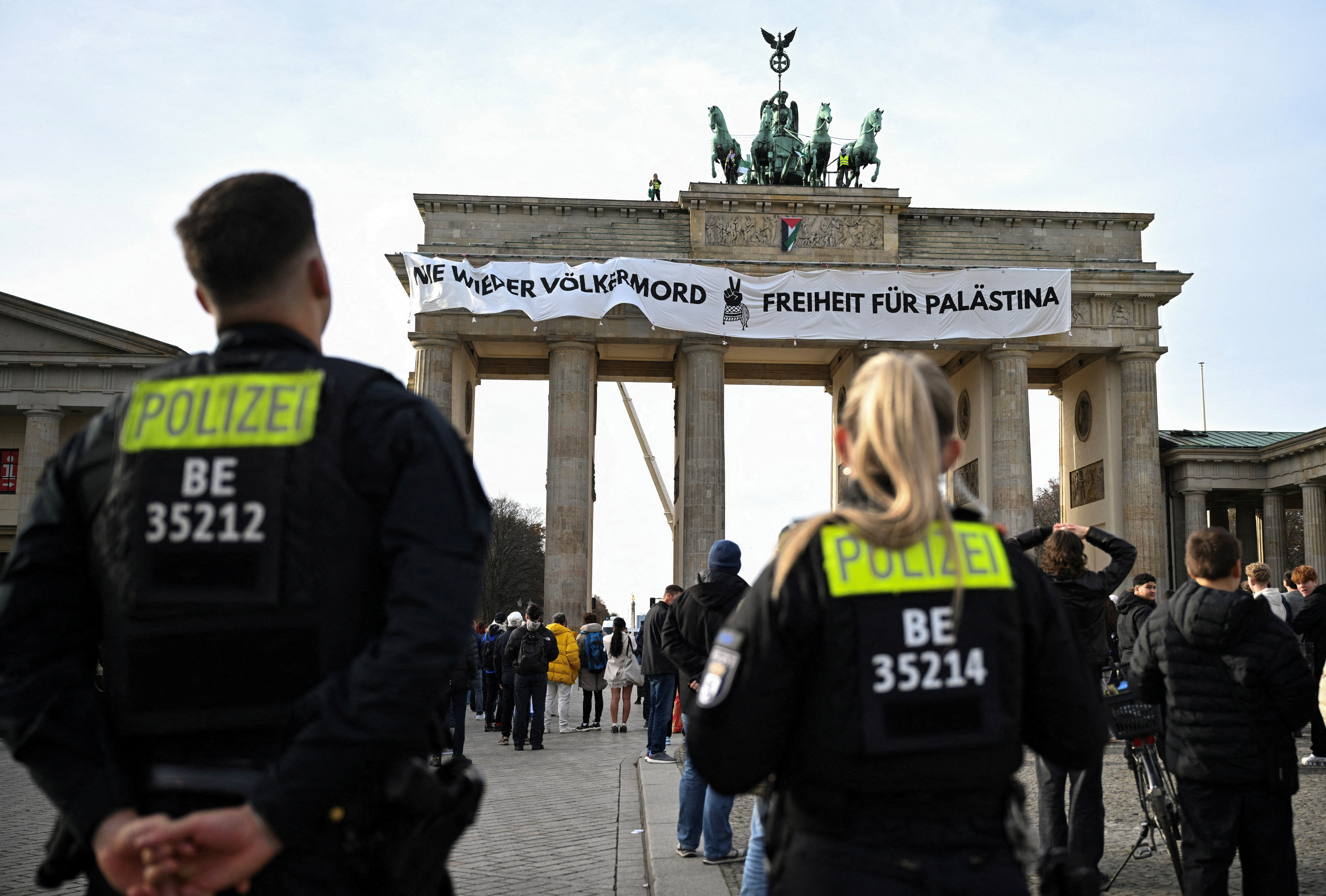 German police officers watch on as pro-Palestinian protesters wave flags and unveil a placard reading, 'Never again genocide - Freedom for Palestine', on top of Brandenburg Gate in Berlin, Germany, November 13, 2025 [Annegret Hilse/Reuters]