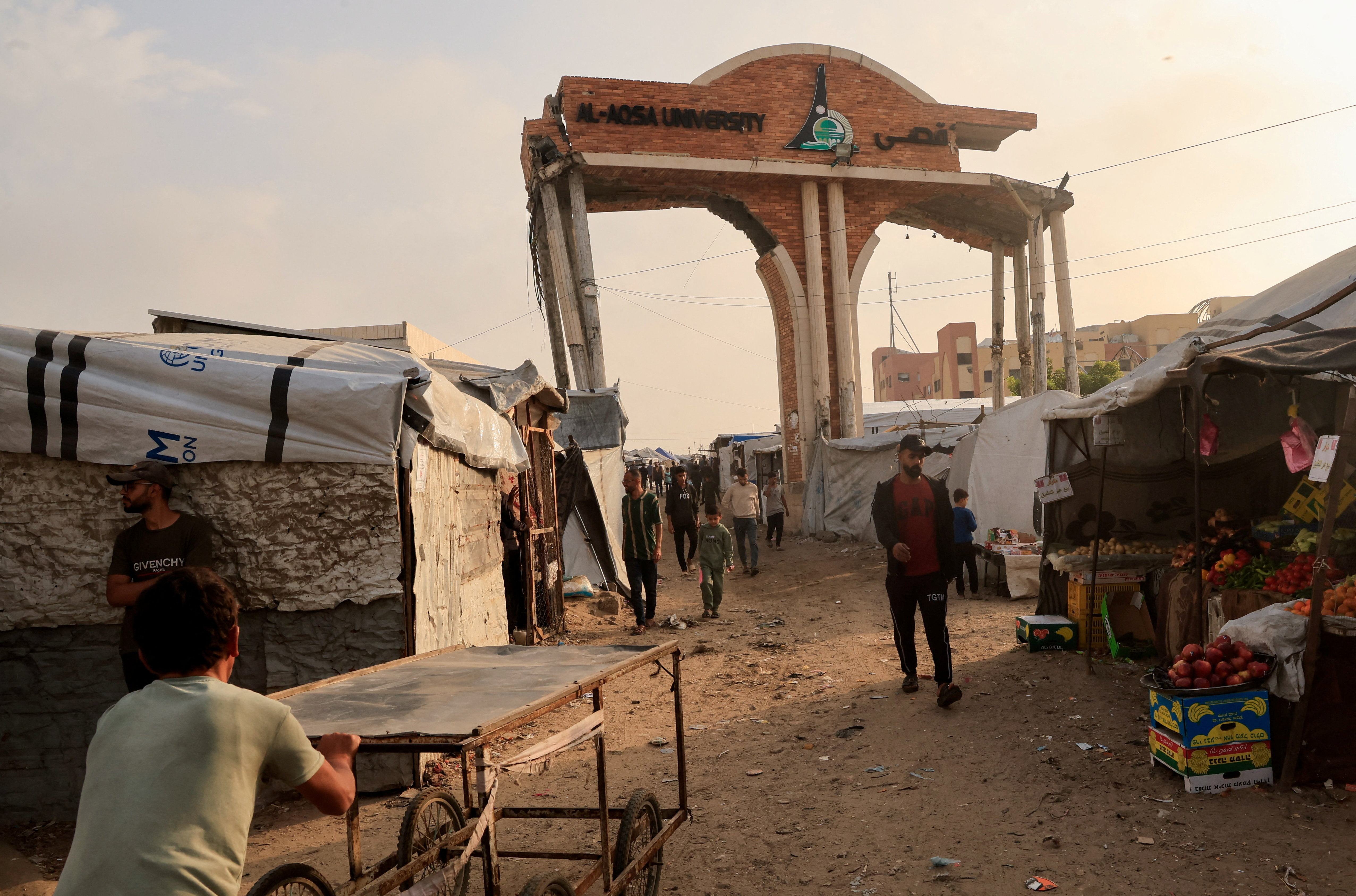 People walk through the damaged gate of Al-Aqsa University surrounded by tents sheltering displaced Palestinians, in Khan Younis, in the southern Gaza Strip, November 24, 2025. REUTERS/Haseeb Alwazeer