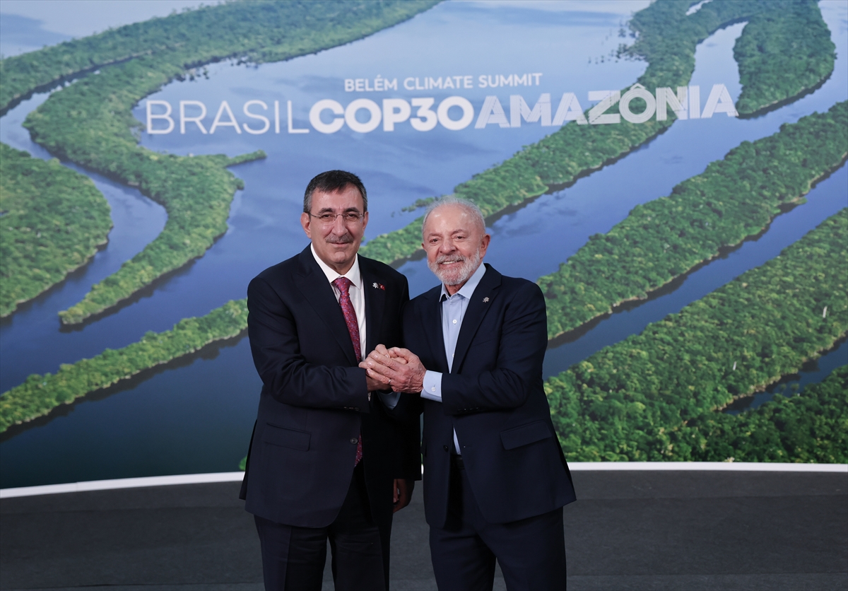 two men shake hands in front of a banner showing an aerial view of the amazon river