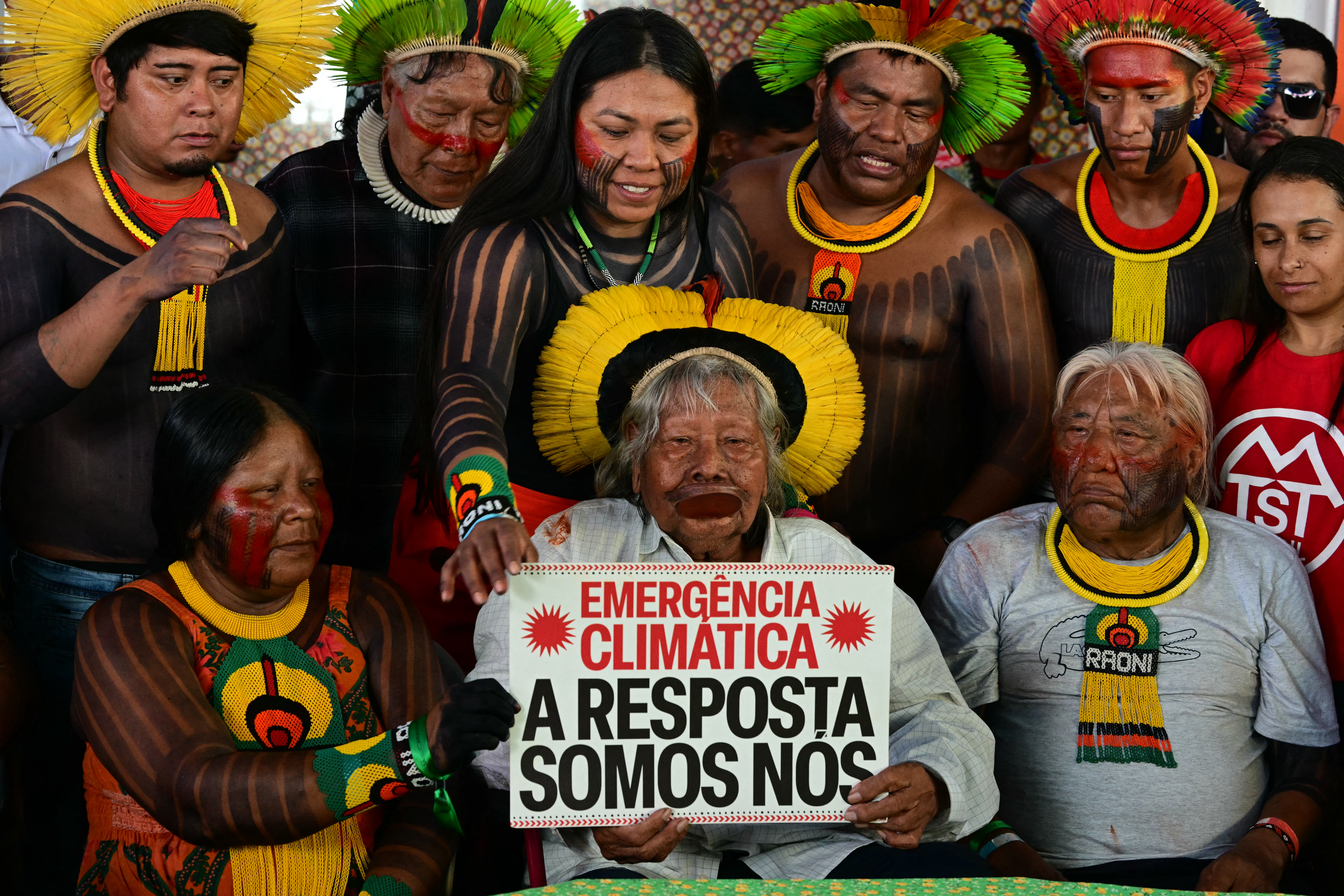 Brazilian Indigenous leader and environmentalist Chief Raoni displays a sign reading 'Climate emergency. The answer is us' during a news conference on board a protest vessel, on the sidelines of the COP30 UN Climate Change Conference in Belem, Para state, Brazil [Pablo Porciuncula/AFP]