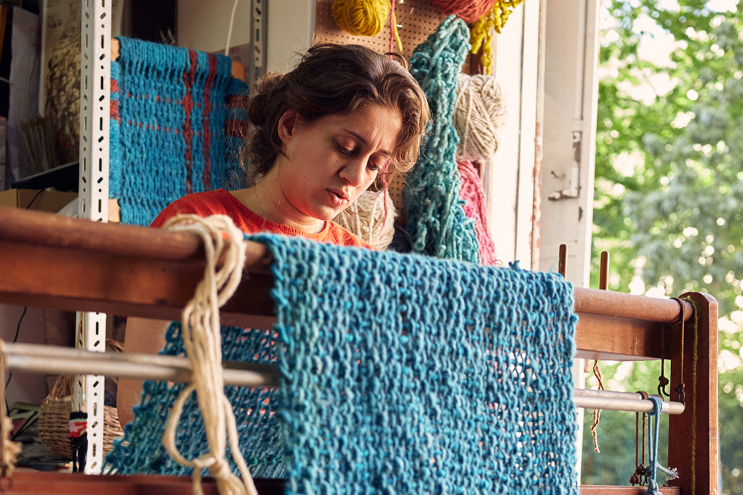 Lara sitting at a traditional loom, turning out a turquoise woven cloth