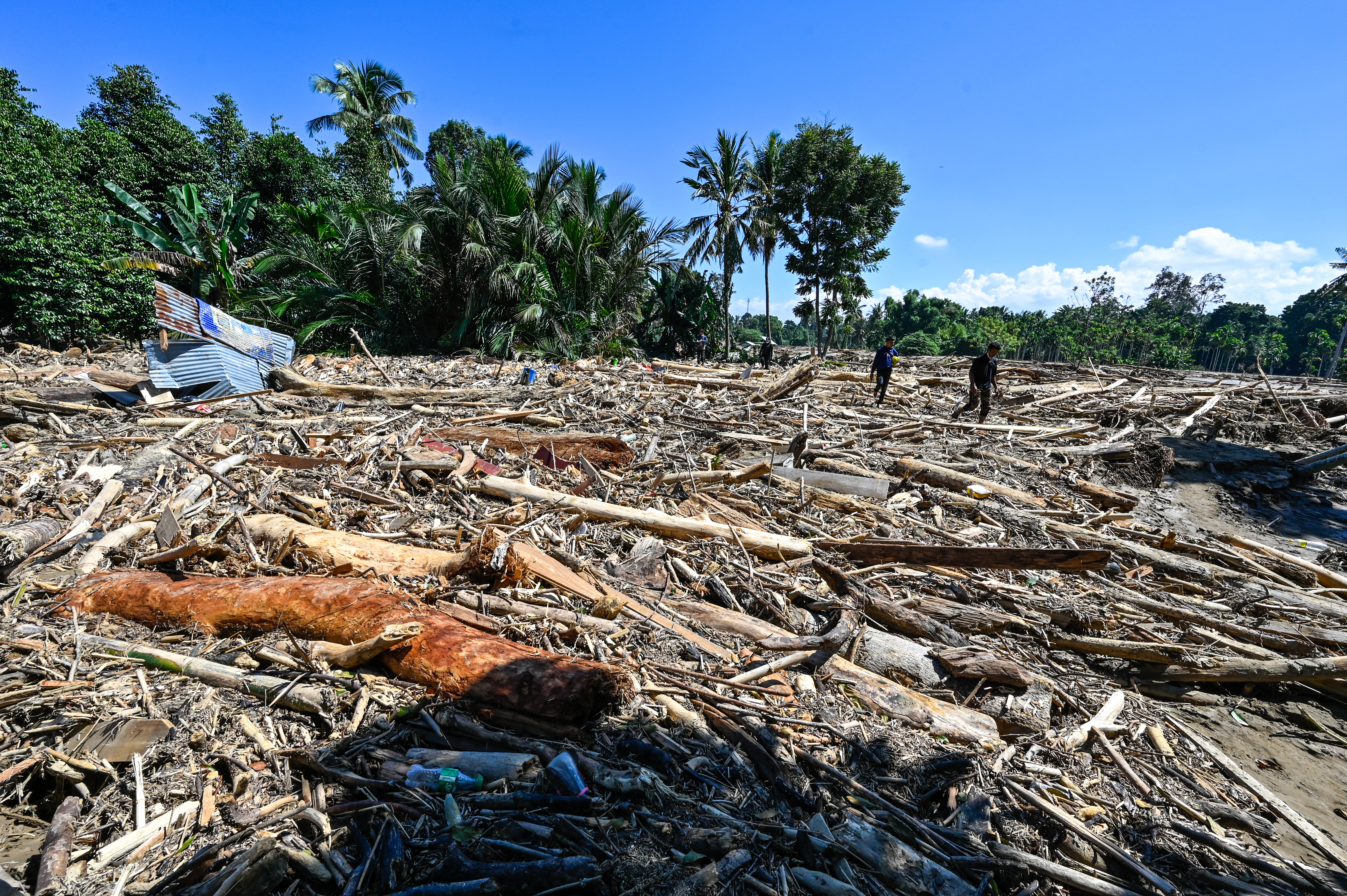 People walk across mud and debris in a flood affected area in Meureudu, Pidie Jaya district in Indonesia's Aceh province on November 30, 2025.