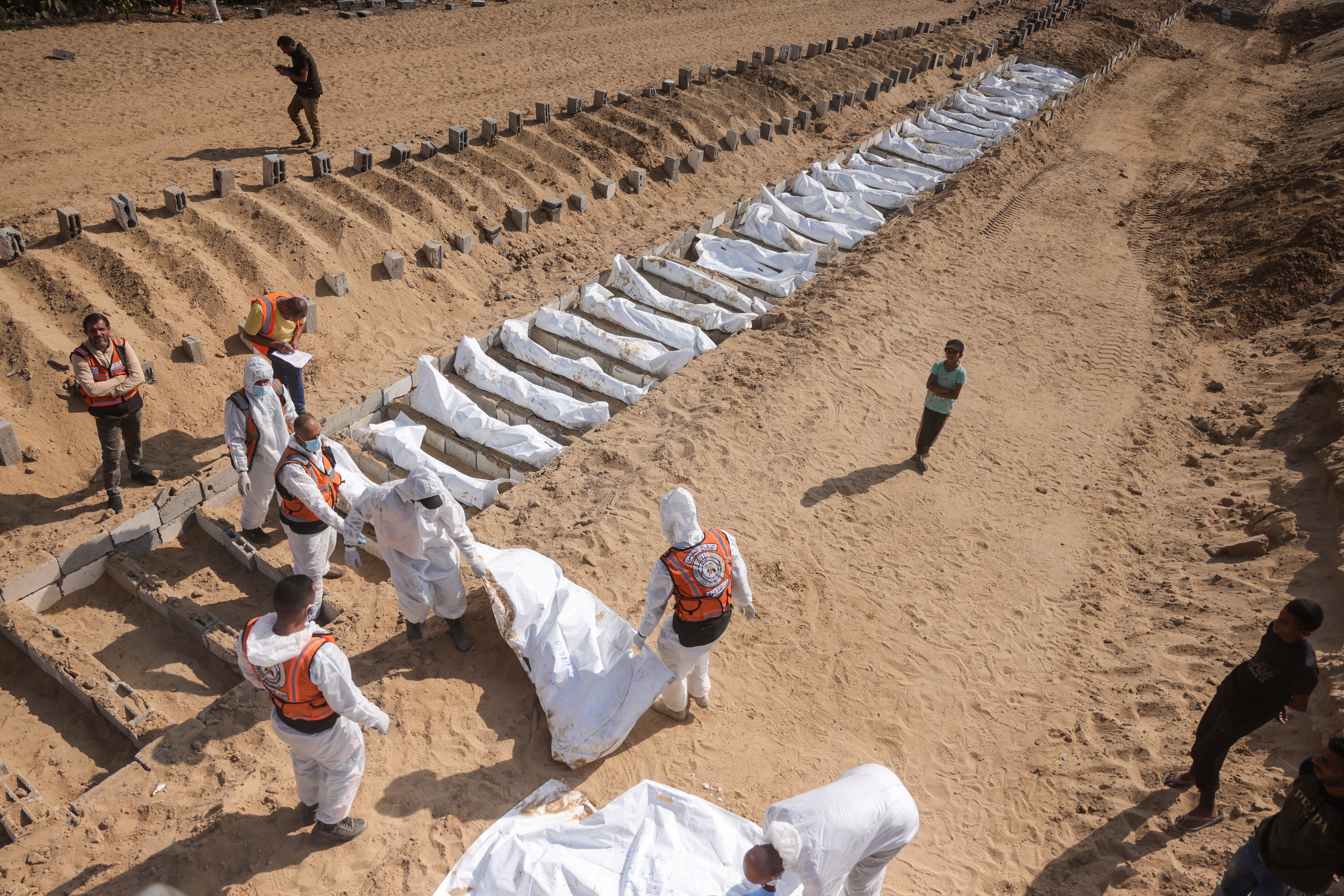 Health and civilian workers conduct a mass burial of Palestinians at a cemetery.