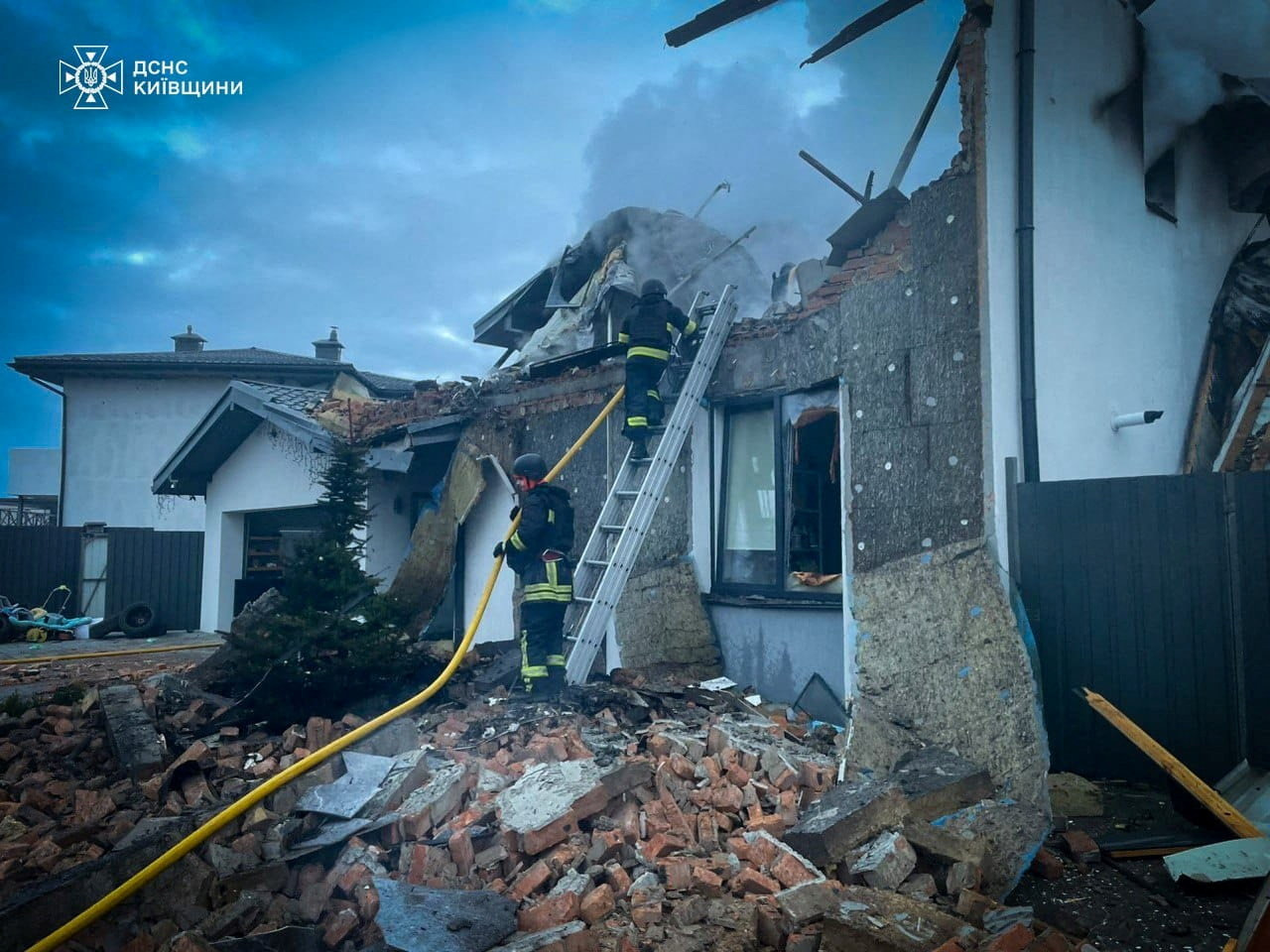 Firefighters work at the site of a heavily damaged house.
