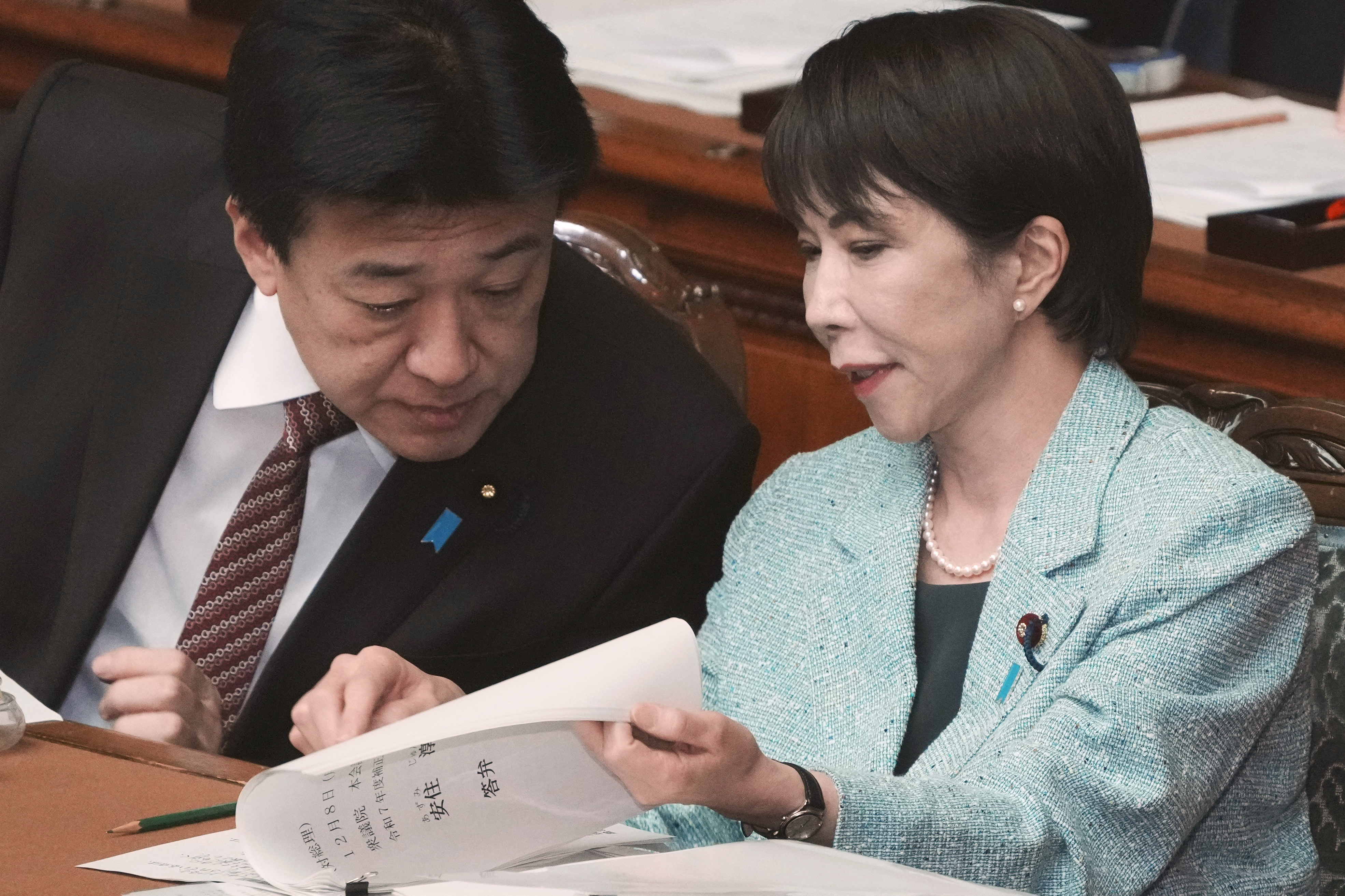 Japan's Prime Minister Sanae Takaichi (R) chats with Chief Cabinet Secretary Minoru Kihara during a plenary session of the House of Representatives at the National Diet in Tokyo