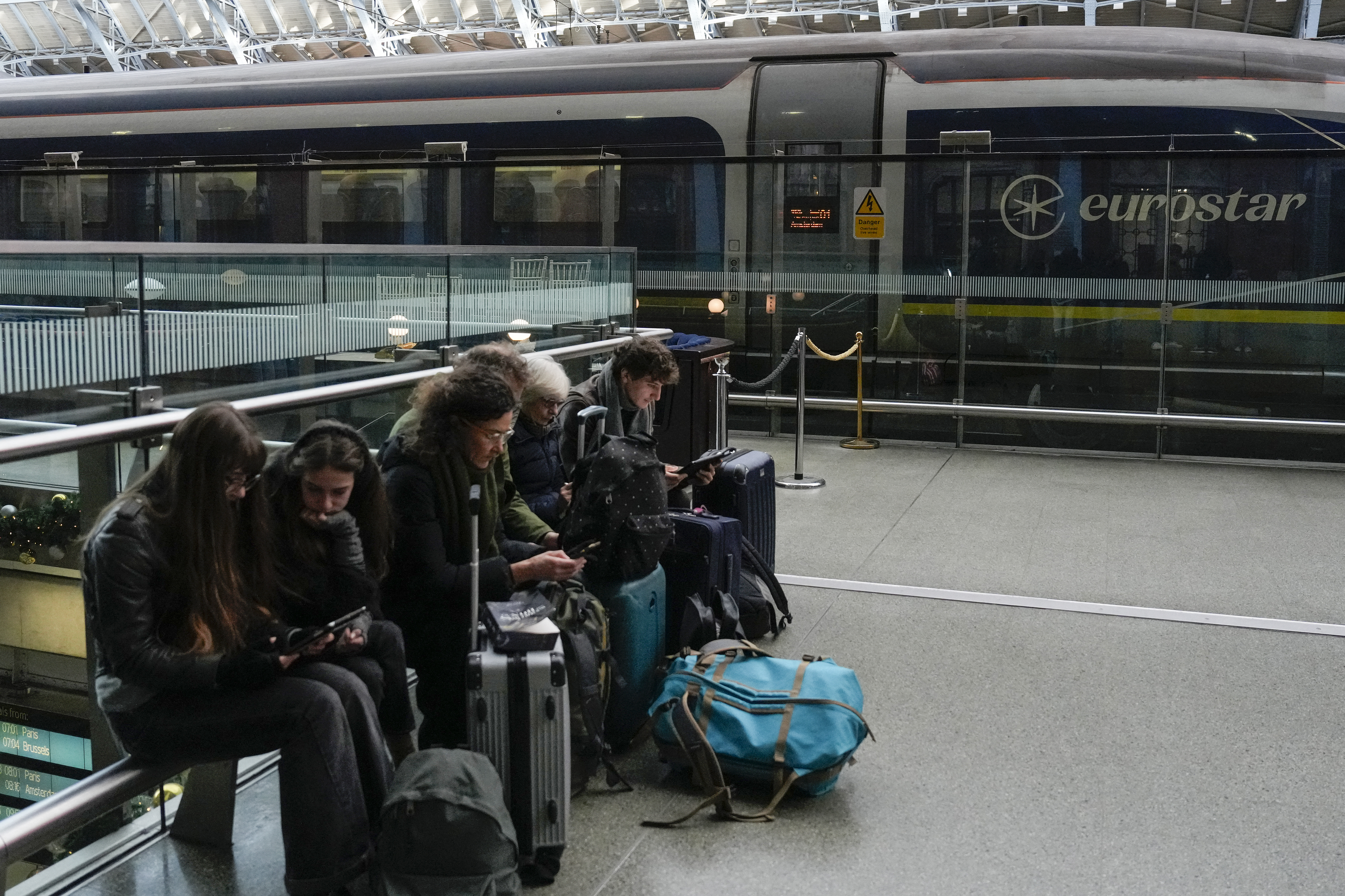 Travellers sit with their bags next to a Eurostar train at St. Pancras station in London on December 30, 2025, as Eurostar train service between Britain and continental Europe is halted.