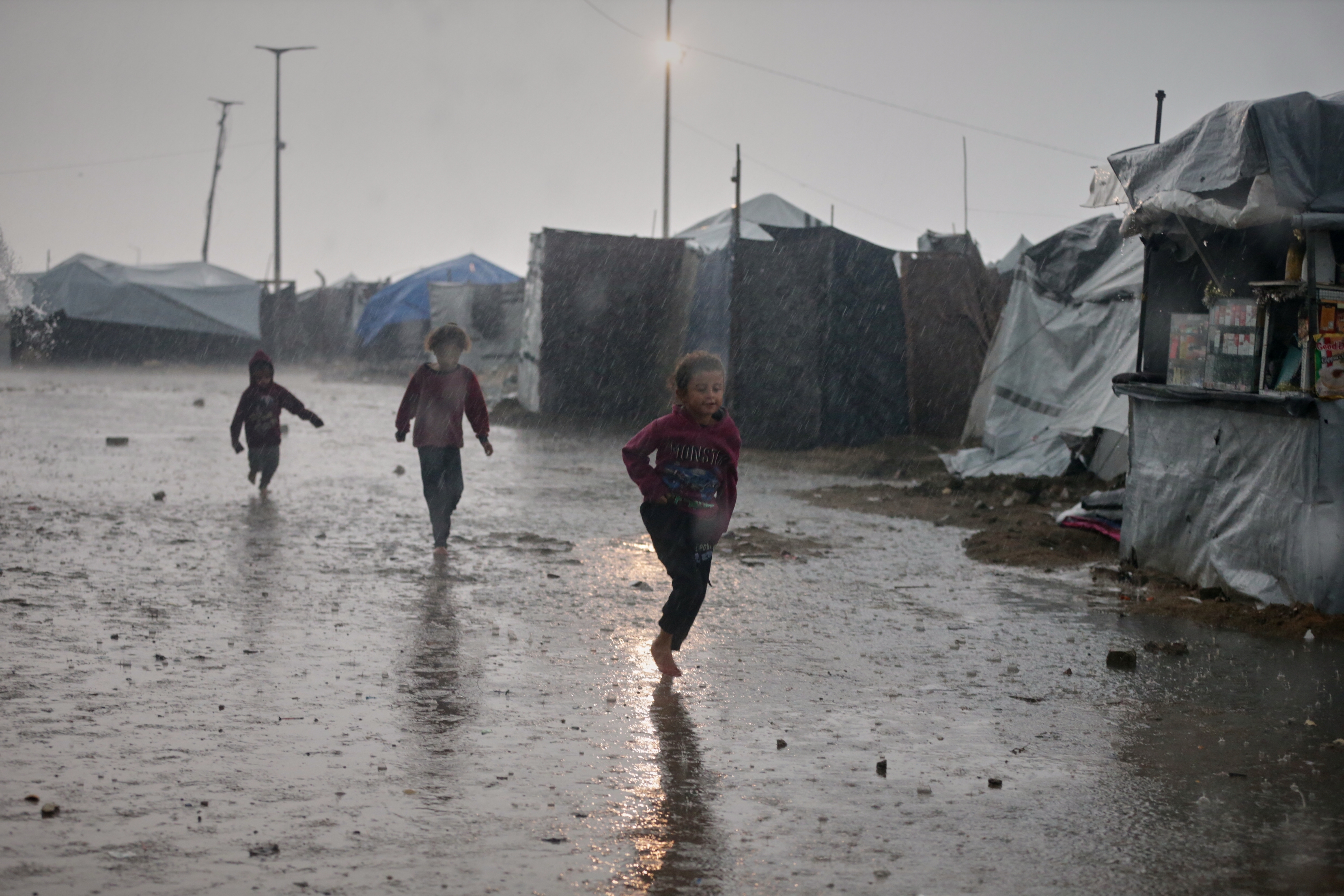 Children run in the rain past a tent camp in Gaza City, Monday, Dec. 15, 2025. (AP Photo/Yousef Al Zanoun)