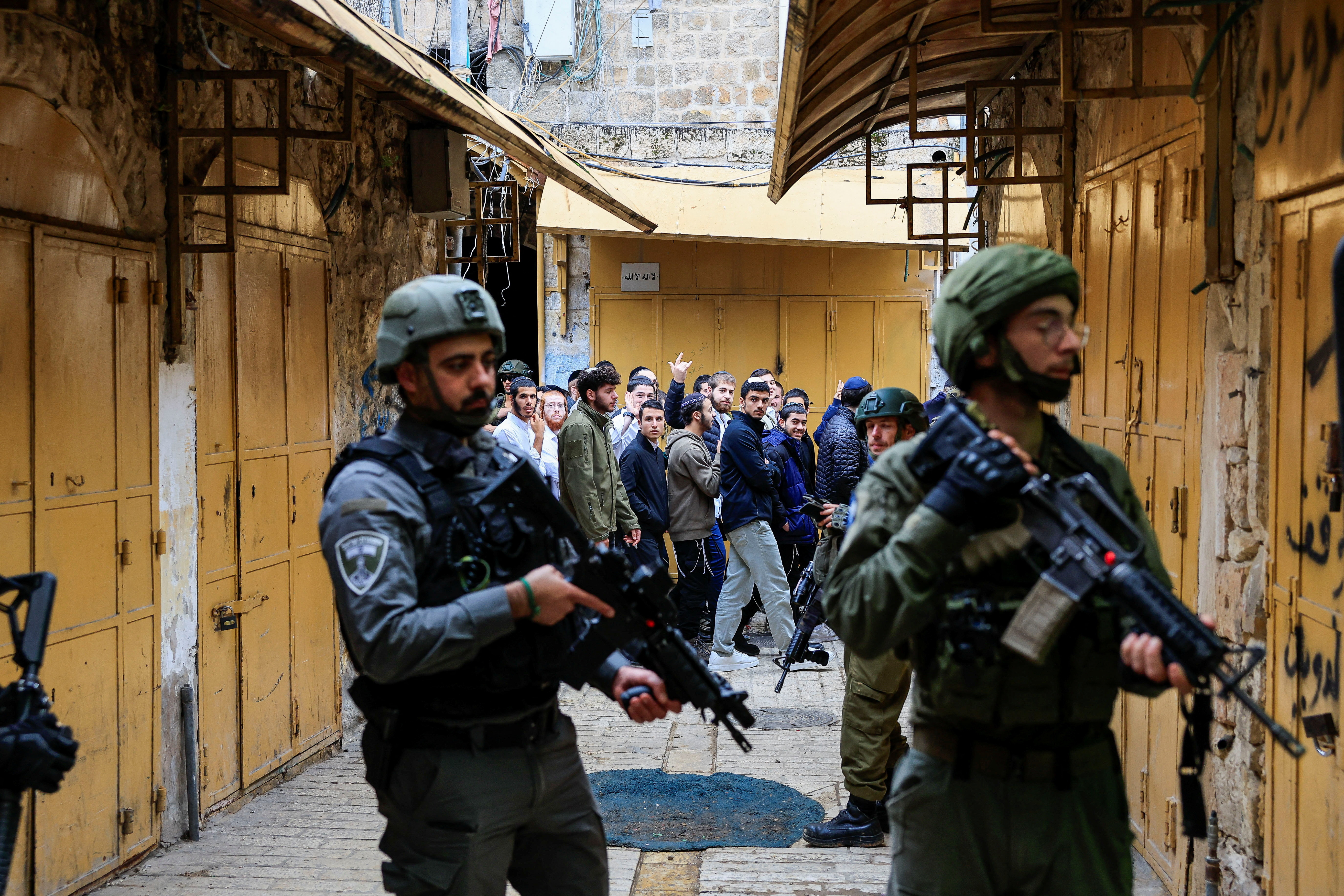 Israelis walk past troops standing guard during a weekly settlers' tour in Hebron, in the Israeli-occupied West Bank, December 13, 2025. REUTERS/Mussa Qawasma