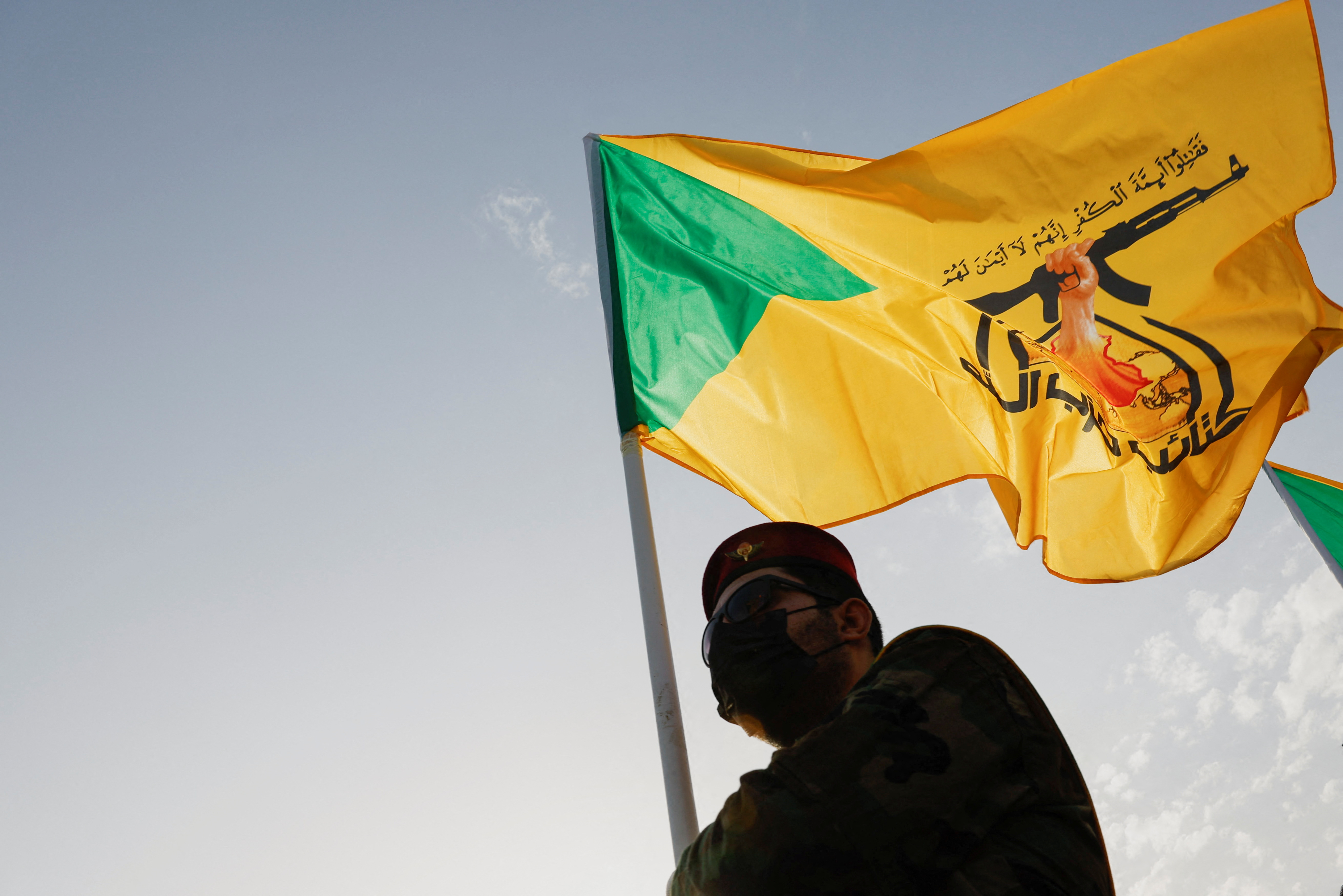 Man stands by yellow Kataib Hezbollah flag
