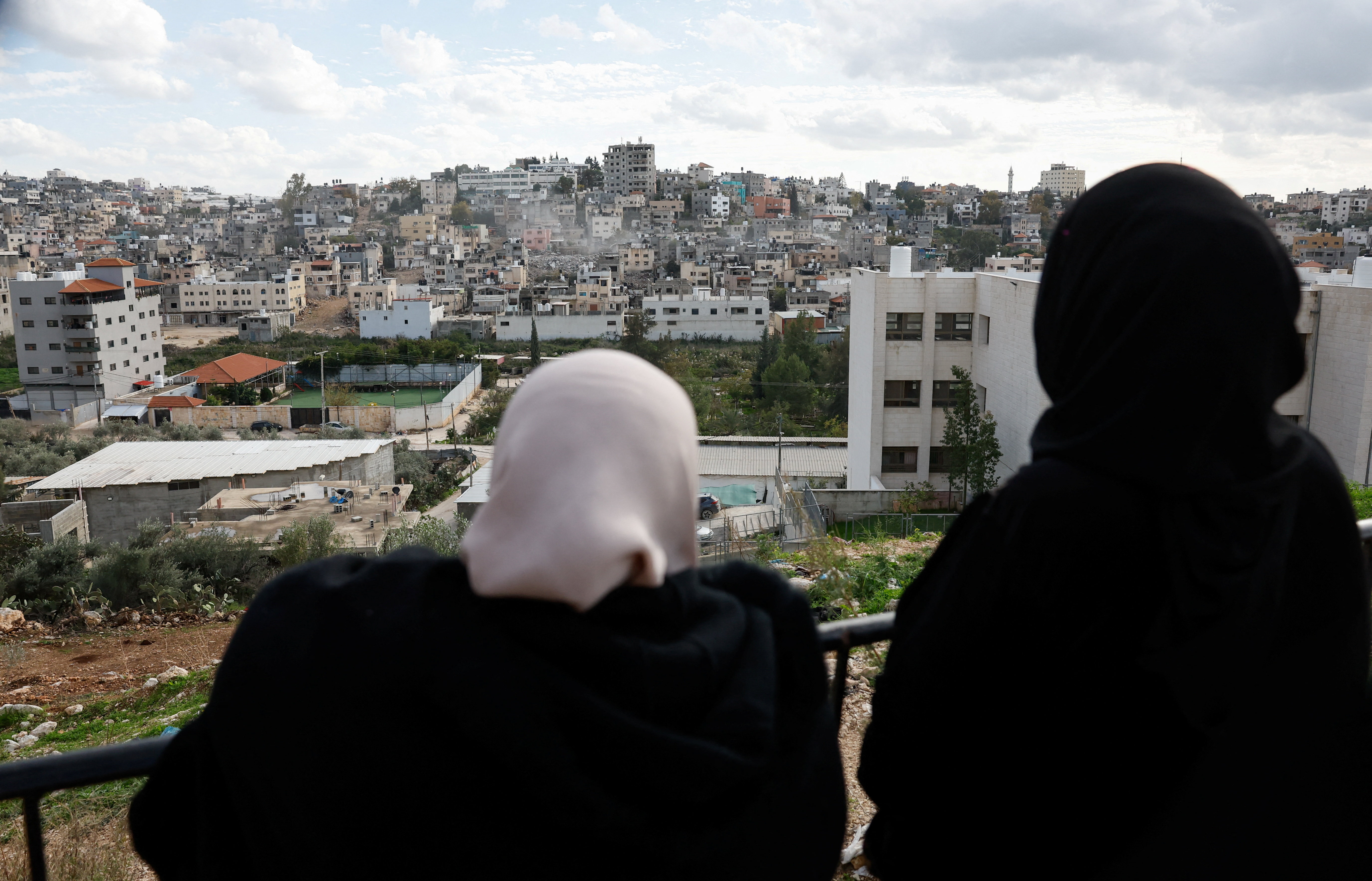 Palestinian women look at Israeli heavy machinery demolishing a Palestinian building at Nur Shams refugee camp in West Bank