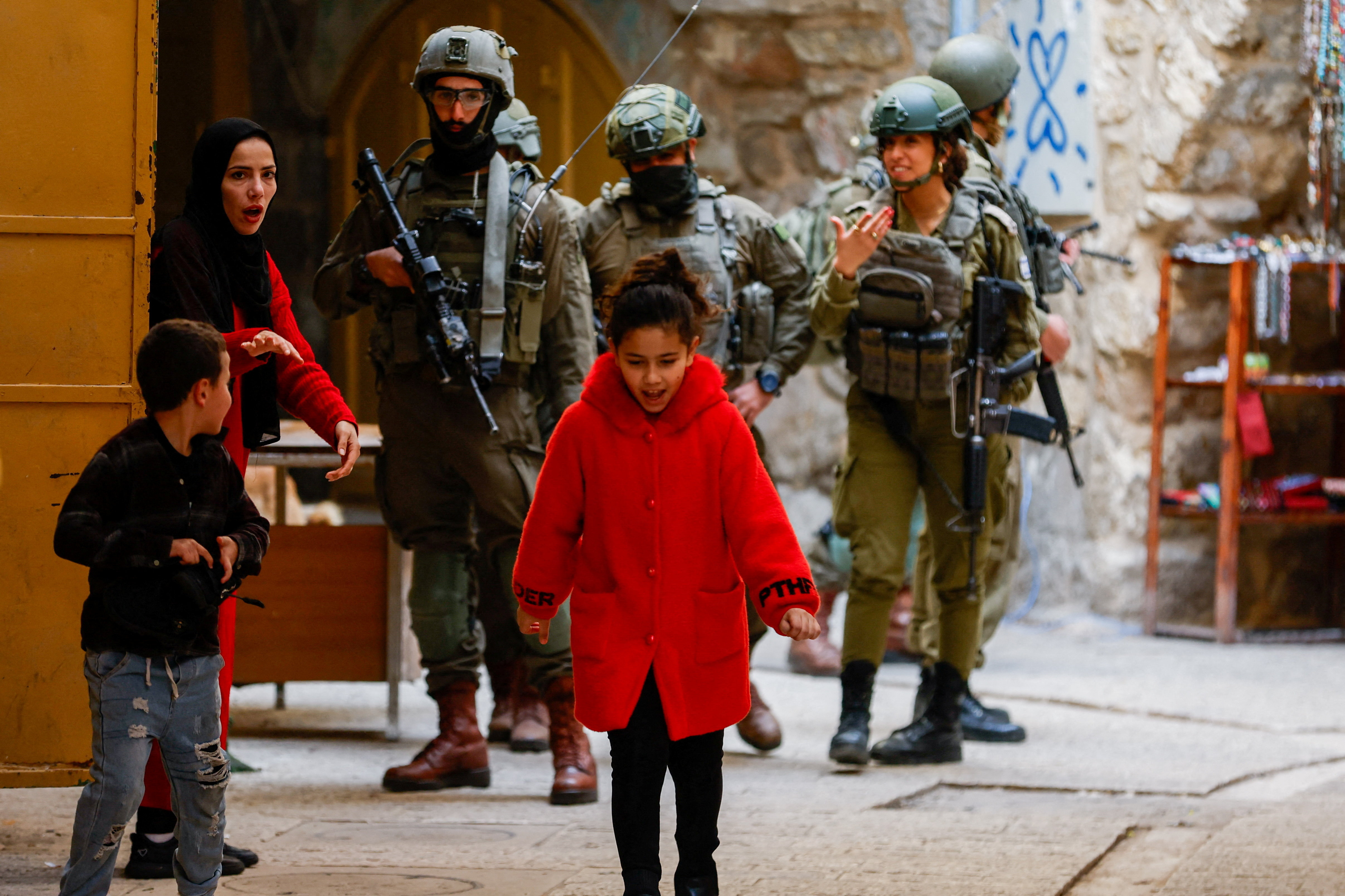 A Palestinian woman ushers her children away from a group of Israeli soldiers during a weekly settlers’ tour in Hebron, in the Israeli‑occupied West Bank, January 24, 2026. REUTERS/Mussa Qawasma TPX IMAGES OF THE DAY
