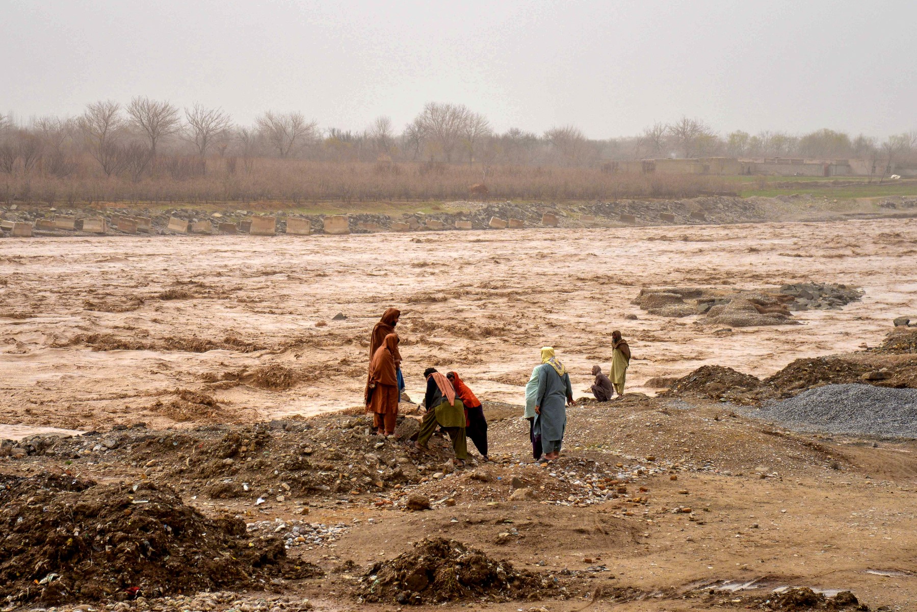 Afghans stand near a river after flash floods at Daman district in Kandahar province on February 26, 2025. Flash floods ripped through western Farah province on February 25, washing away 21 people, while three more were killed when a hail storm caused their house to collapse. Further east, six people were killed in Helmand province, including a child struck by lightning, and nine in Kandahar province. (Photo by Sanaullah SEIAM / AFP)