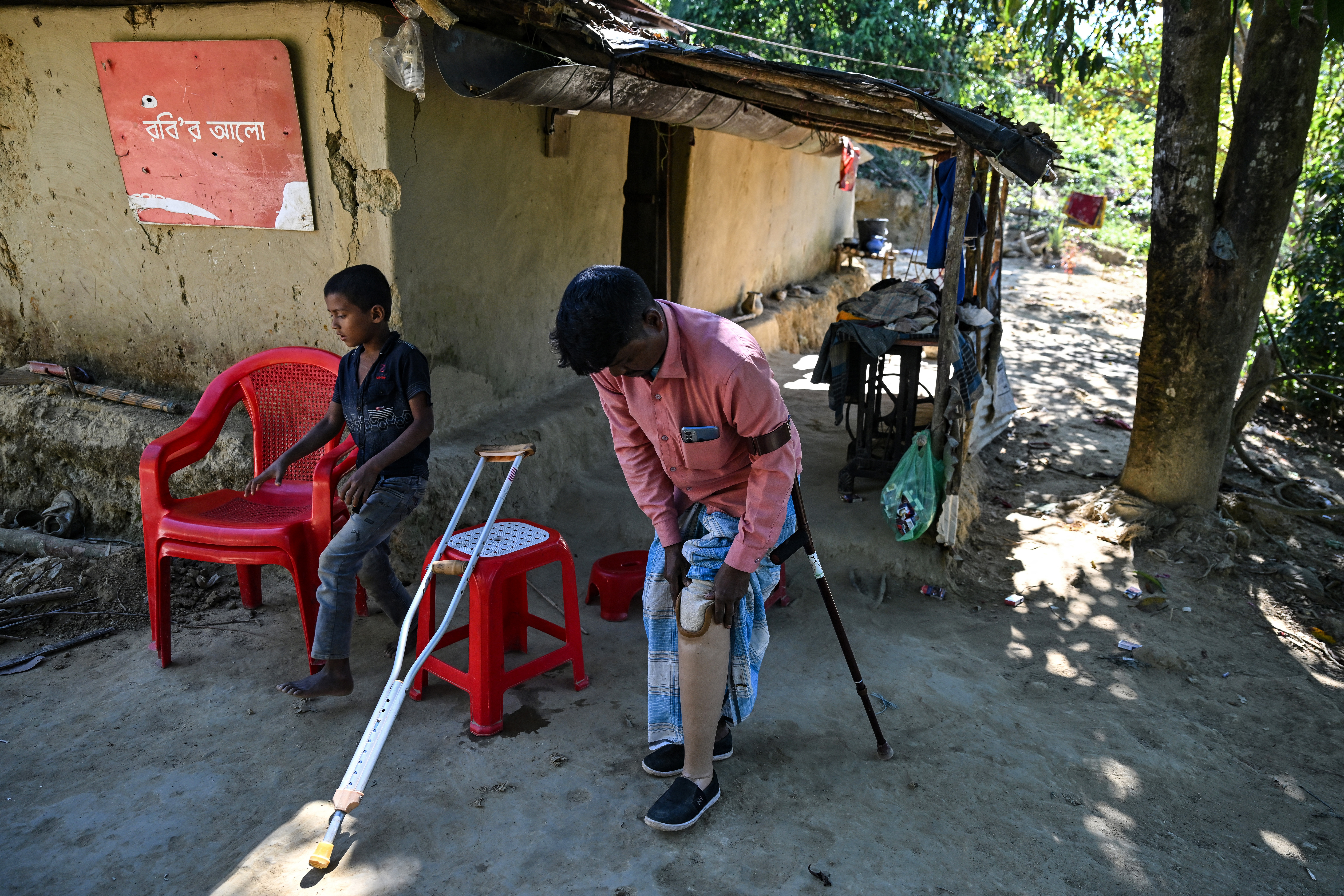 A man leans on a crutch as he removes his prosthetic leg outside his house.