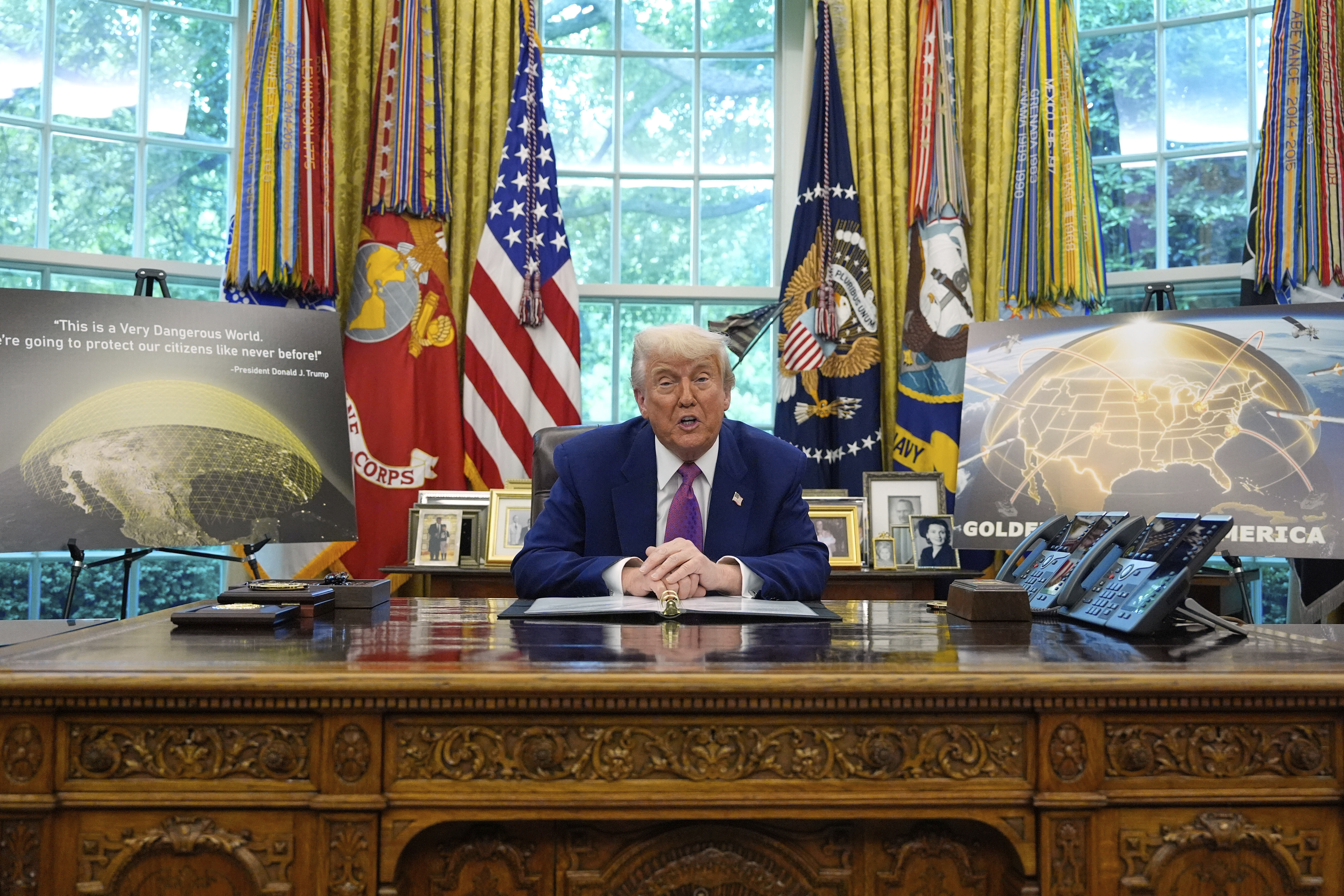 Donald Trump sits between signs for the Golden Dome