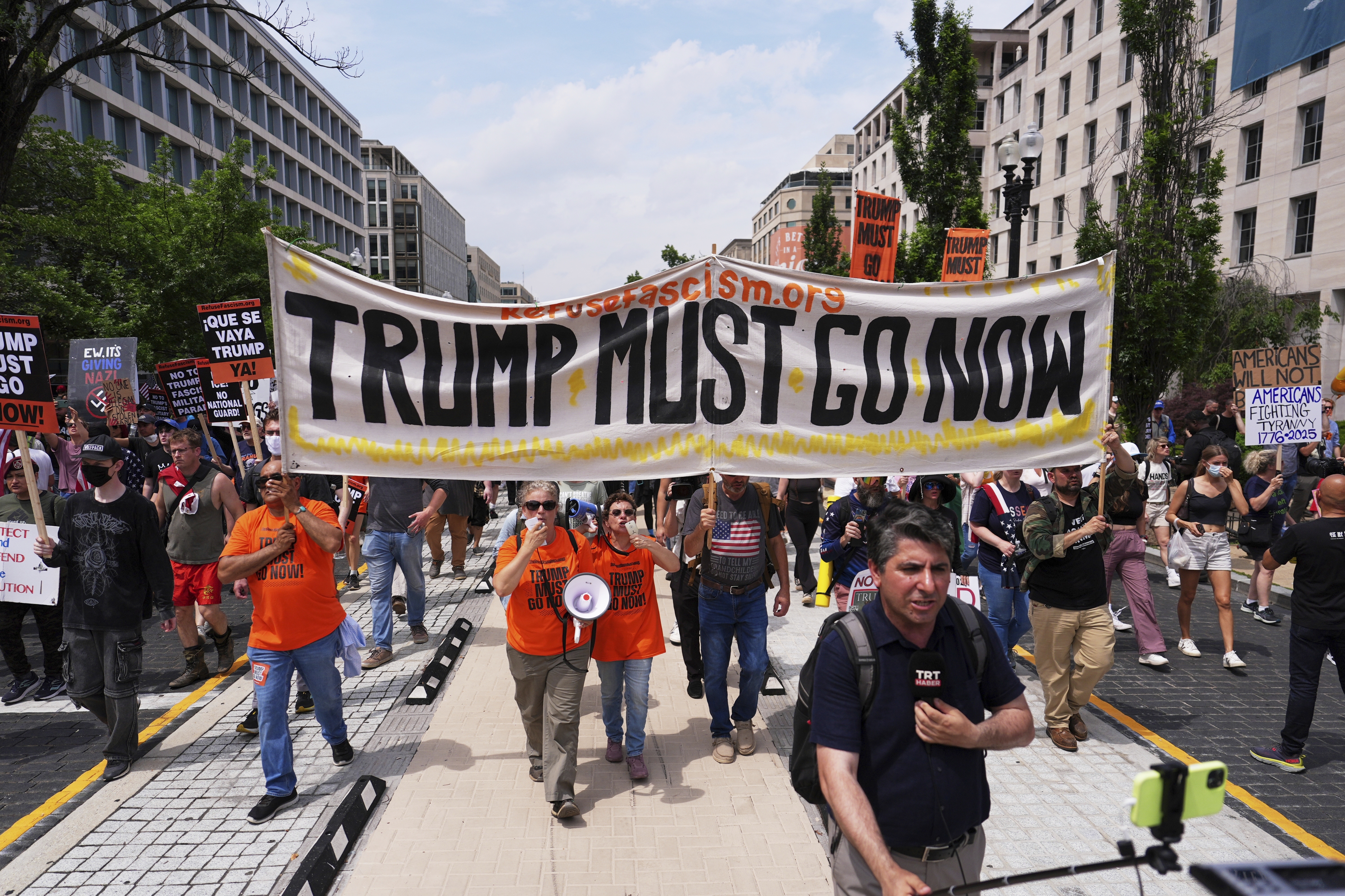 Protesters hold a banner that says, "Trump must go now"