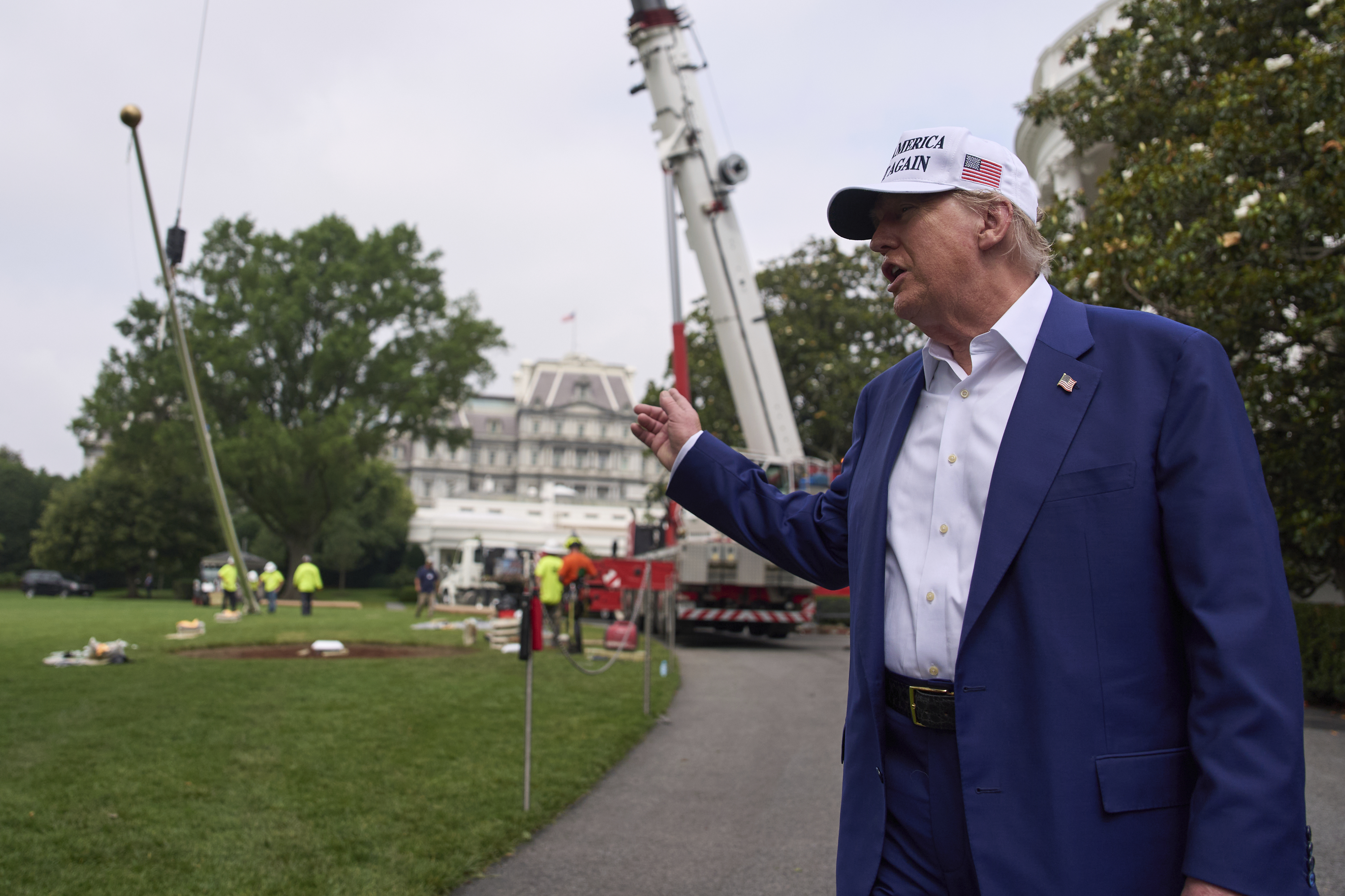 Trump points at a crane erecting a giant flag pole on the White House lawn.