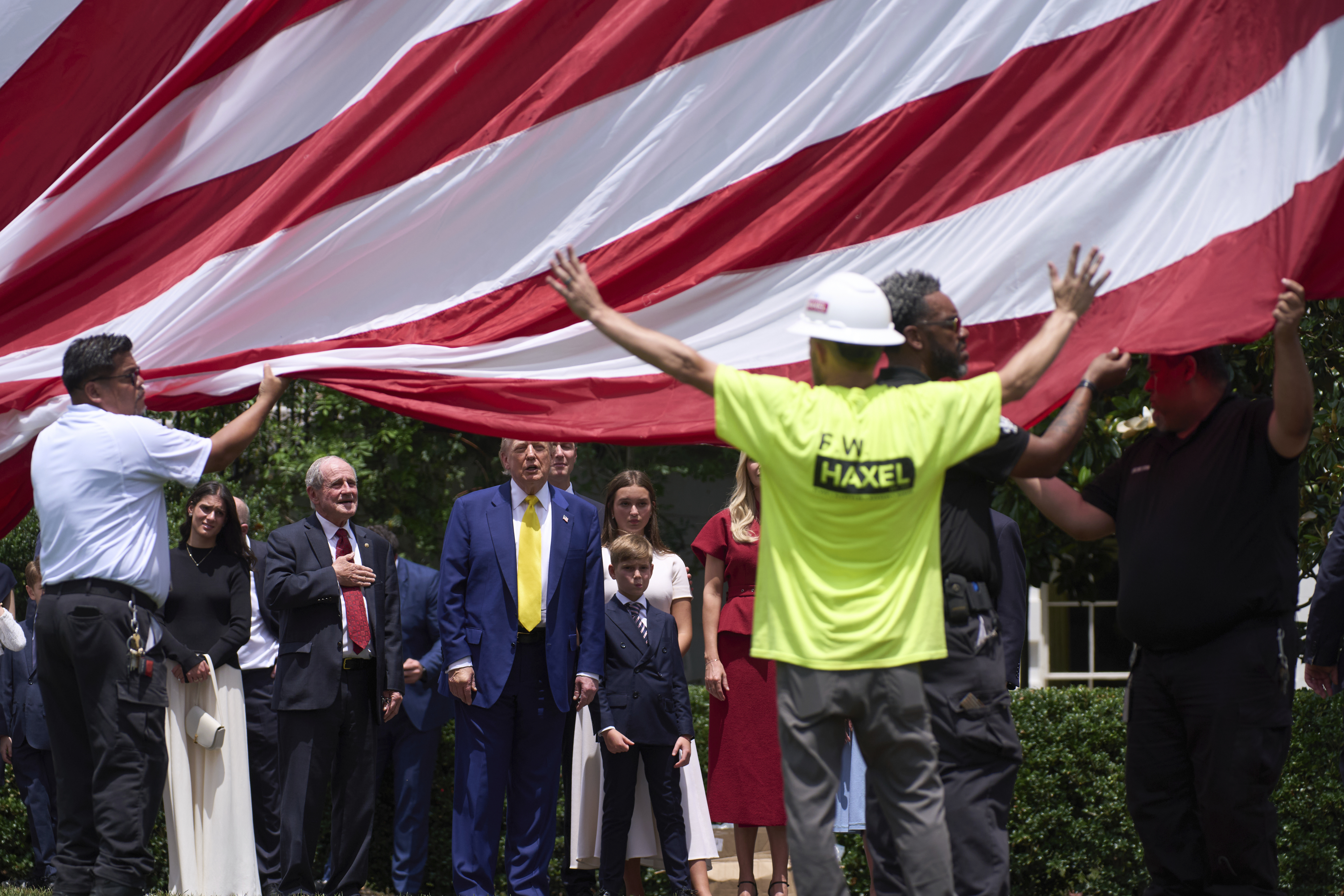 Construction workers raise a giant flag as Trump looks on