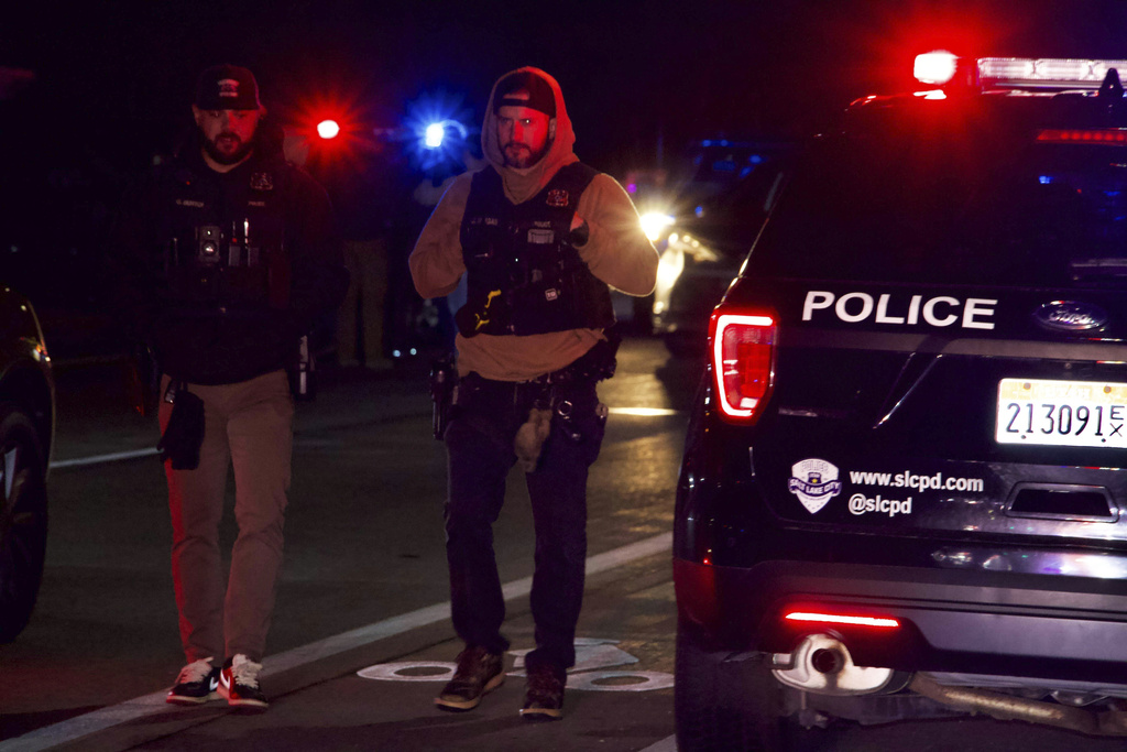 Policemen stand next to police vehicles.
