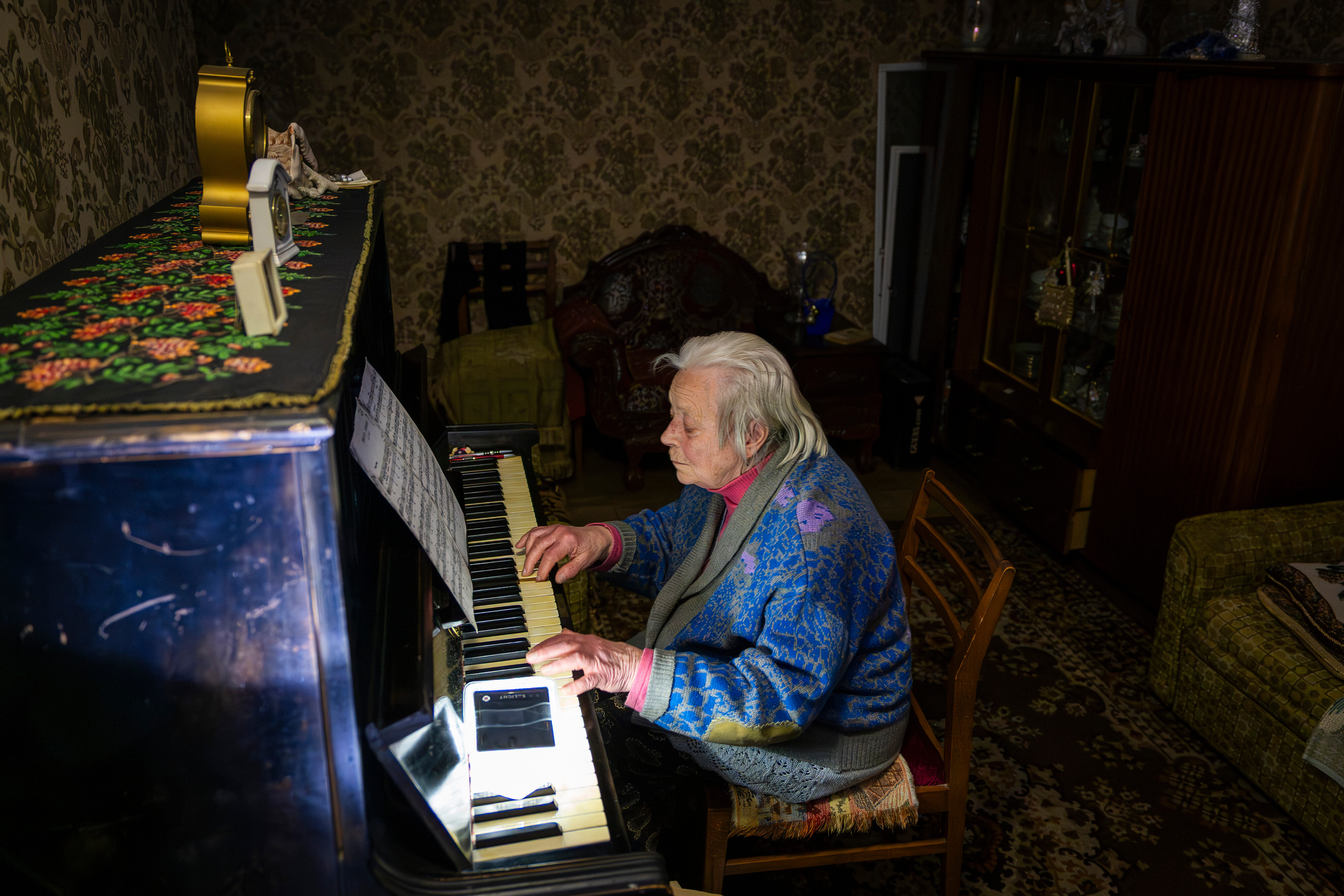 An elderly woman plays a piano in the dark.