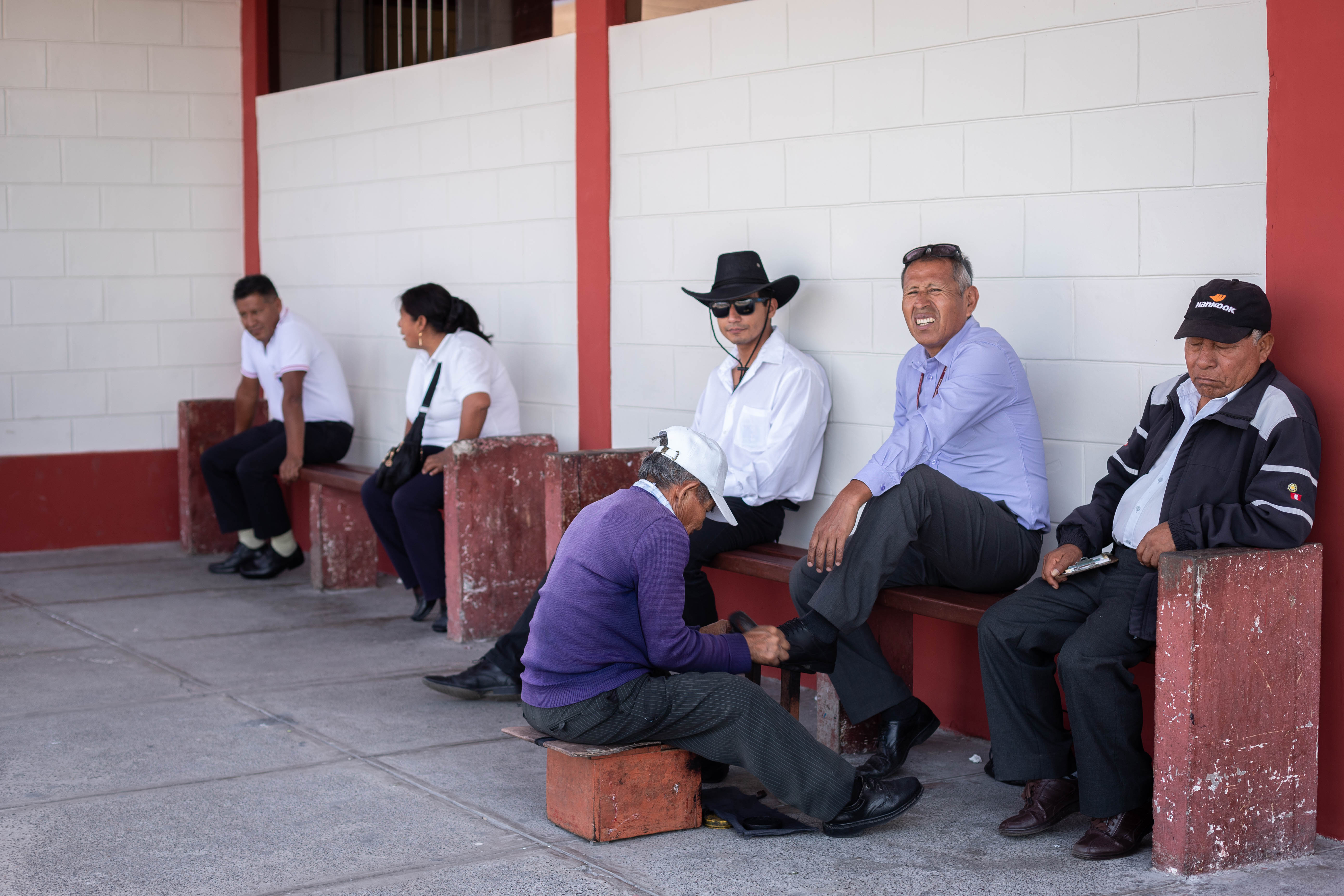 Men sit on a bench while one gets his shoes shined