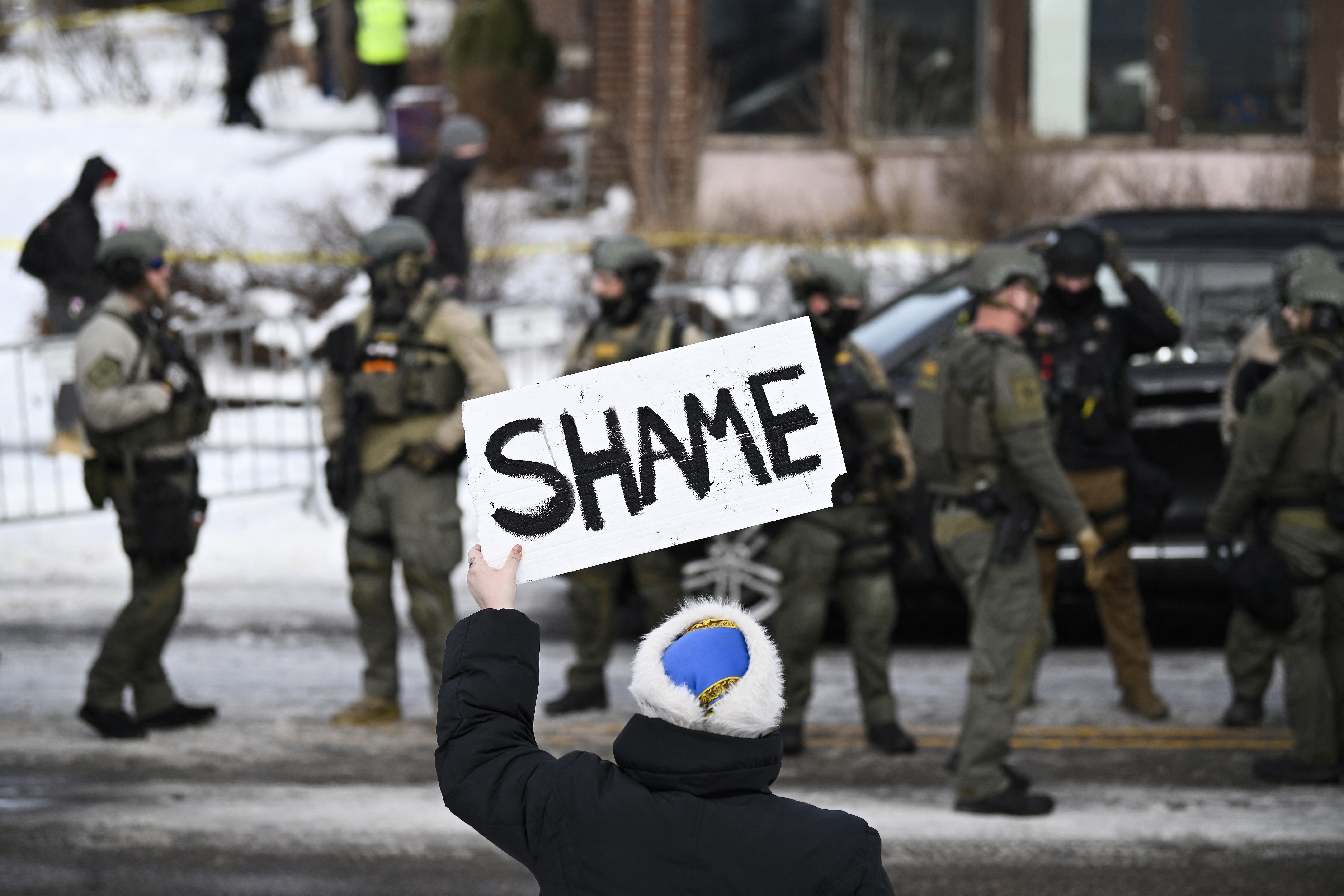 MINNEAPOLIS, MINNESOTA - JANUARY 07: An onlooker holds a sign that reads "Shame" as members of law enforcement work the scene following a suspected shooting by an ICE agent during federal law enforcement operations on January 07, 2026 in Minneapolis, Minnesota. According to federal officials, the agent, “fearing for his life” killed a woman during a confrontation in south Minneapolis. Stephen Maturen/Getty Images/AFP (Photo by Stephen Maturen / GETTY IMAGES NORTH AMERICA / Getty Images via AFP)