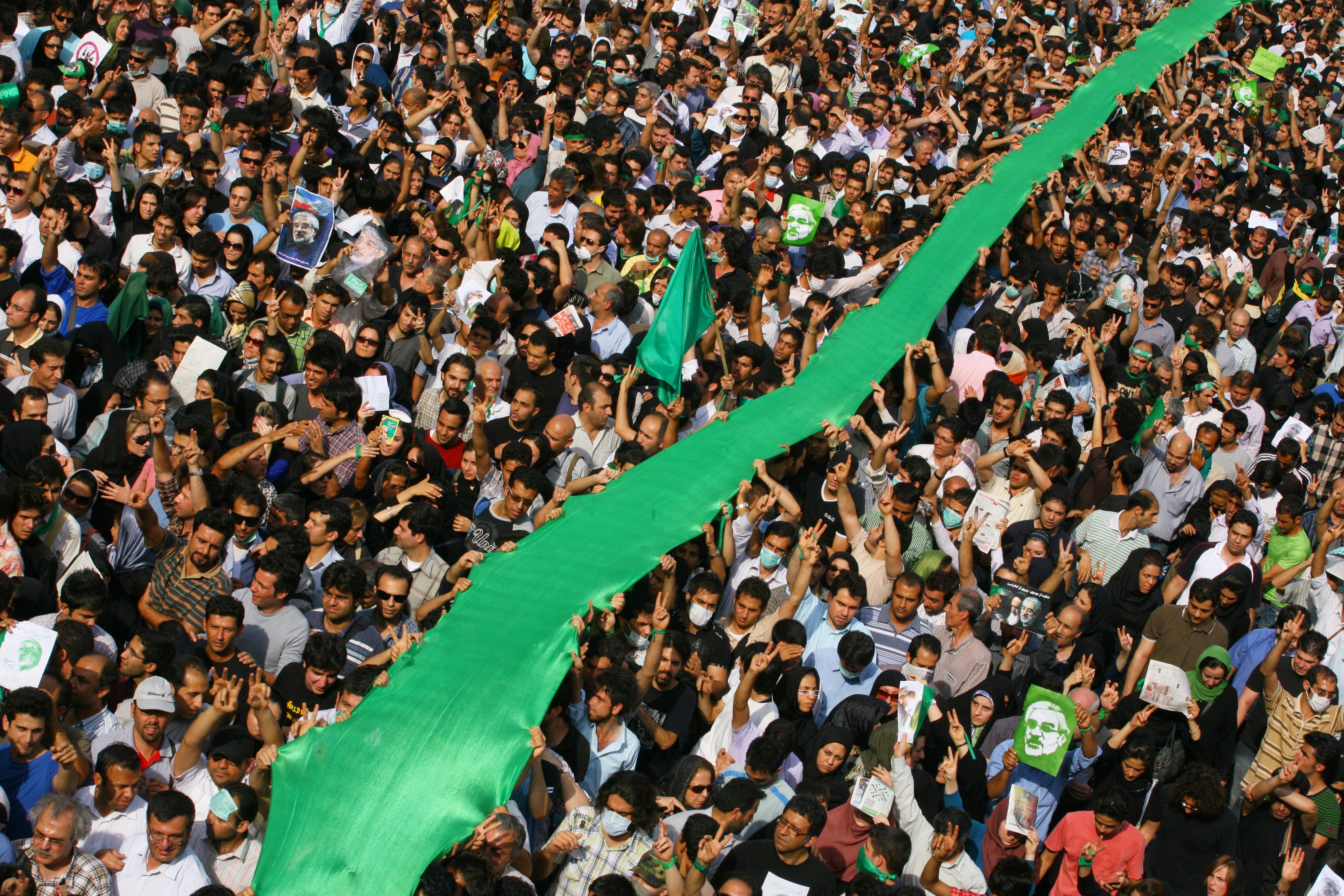 TEHRAN, IRAN - JUNE 15: Iranian supporters of defeated reformist presidential candidate Mir Hossein Mousavi carry a large green flag through the crowd as they demonstrate in the streets on June 15, 2009 in Tehran, Iran. Crowds of people gathered to protest the re-election of Iran's President Mahmoud Ahmadinejad, who won a second four-year term in a landslide election victory on June 12. (Photo by Getty Images)