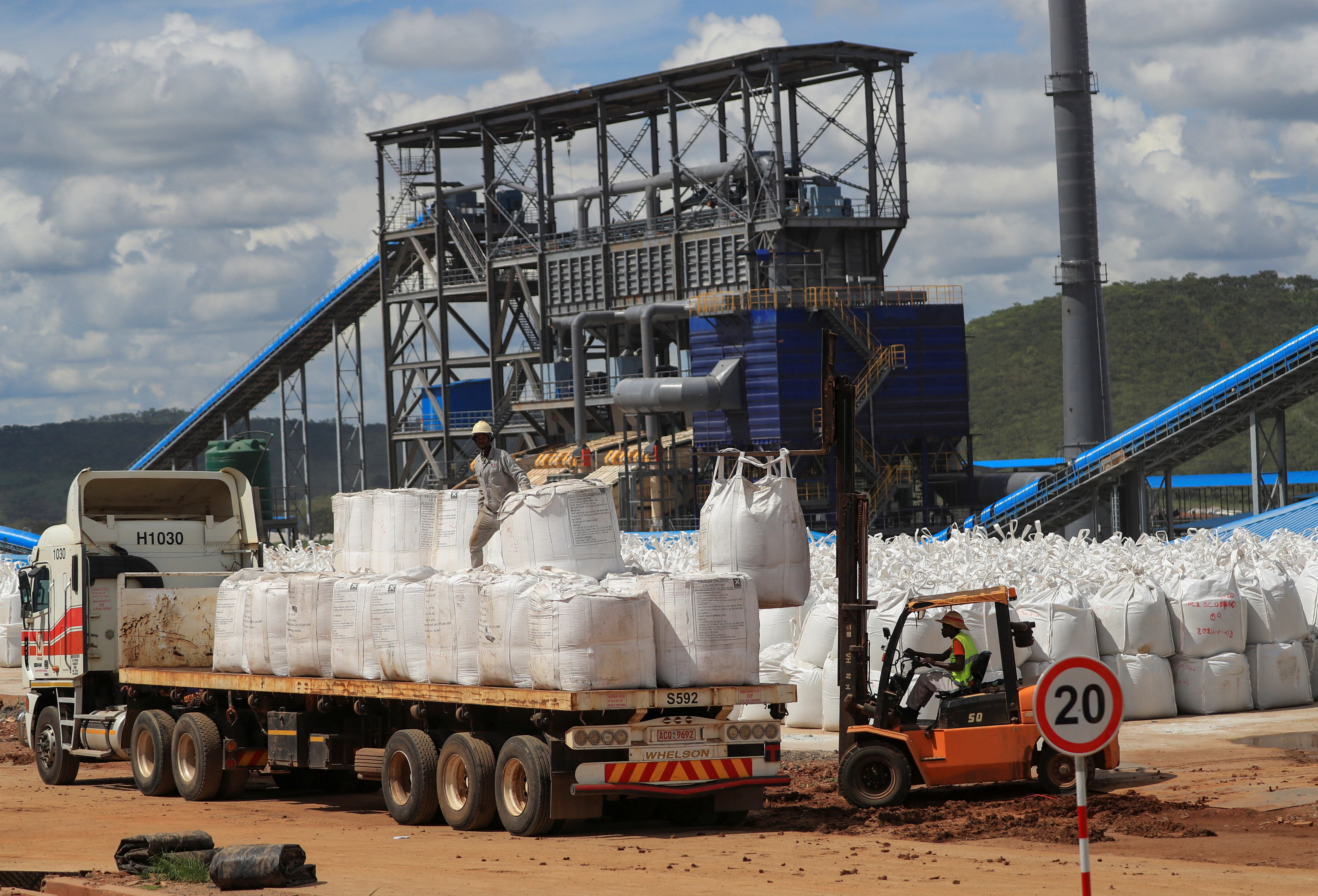 Workers load white bags onto a truck.