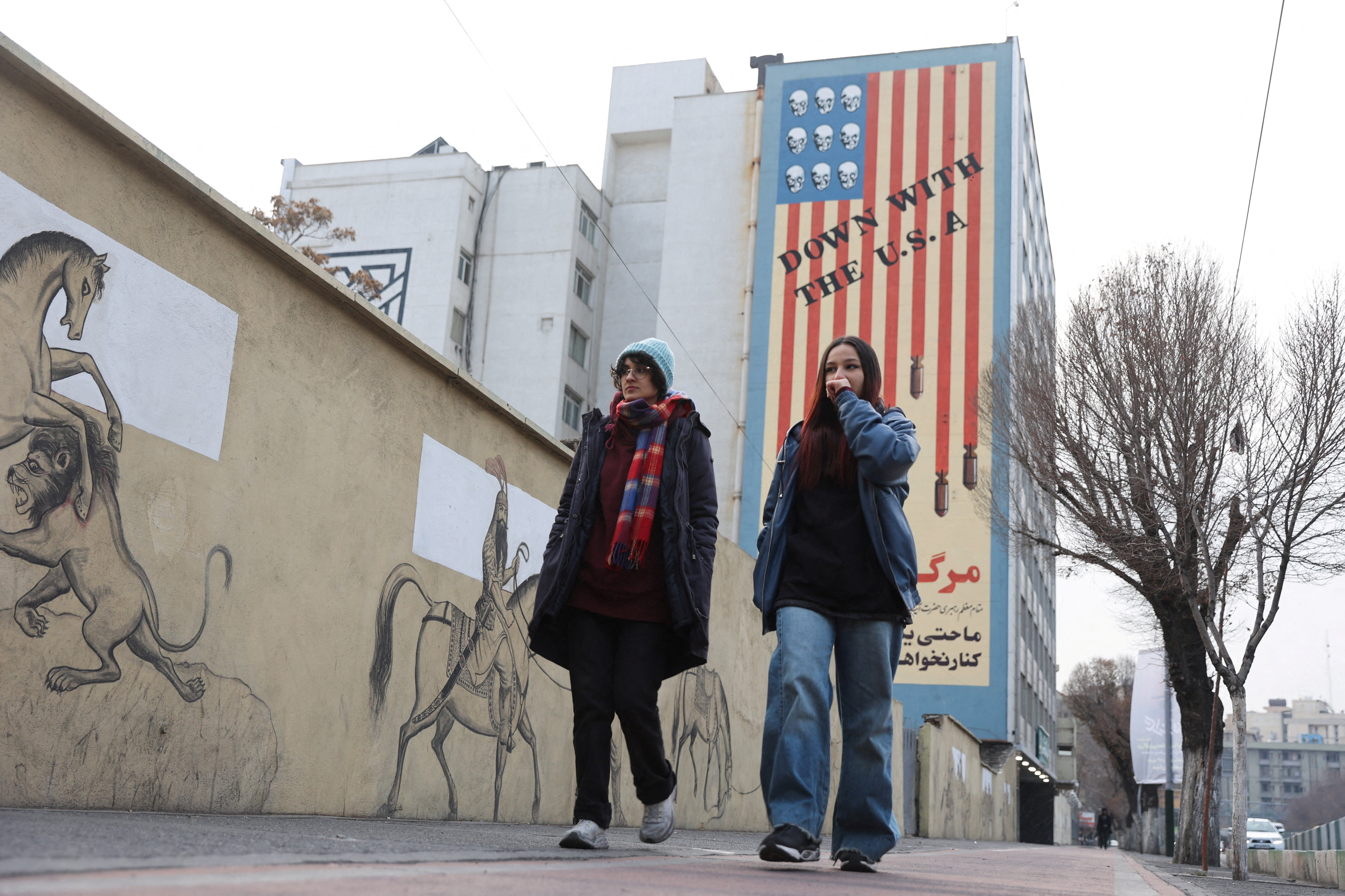 Two people walk past an anti-US mural in Tehran