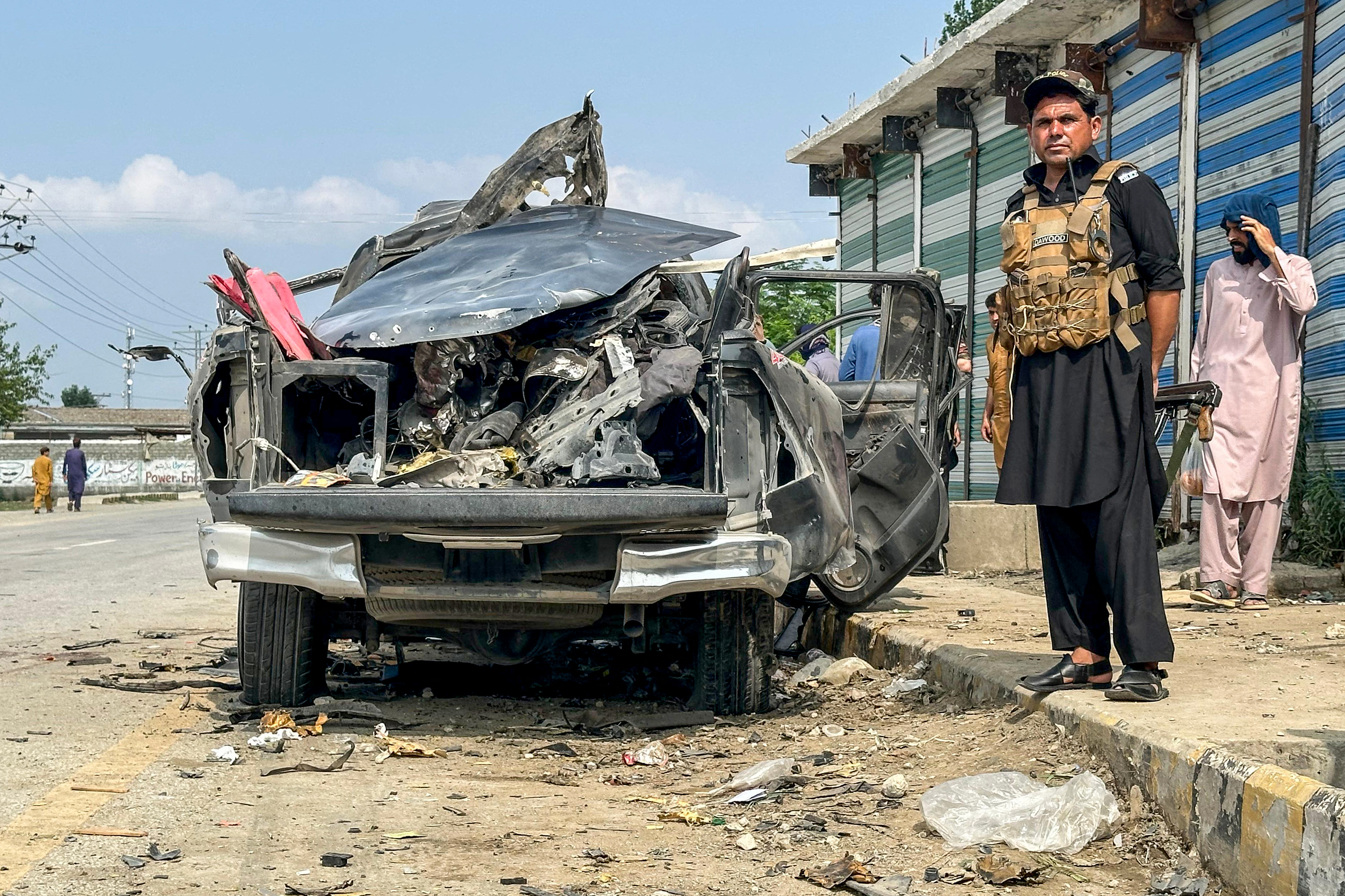 A security person stands guard beside the wreckage of a vehicle after a blast in Bajaur, Khyber Pakhtunkhwa province of Pakistan, in July 2025