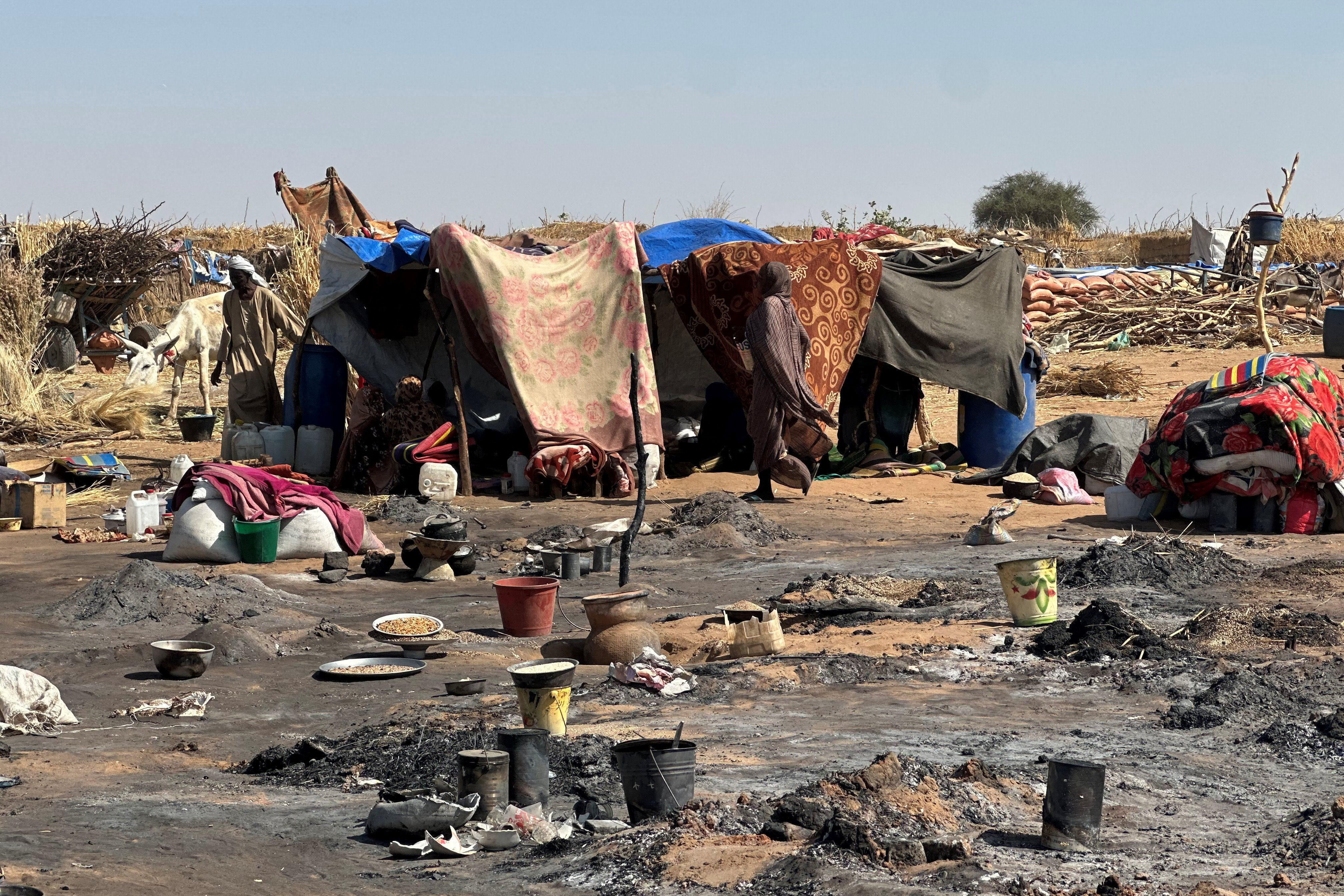 A displaced Sudanese woman who left El-Fasher after its fall with others, walks amid the remains of a fire that broke out at a camp in Tawila