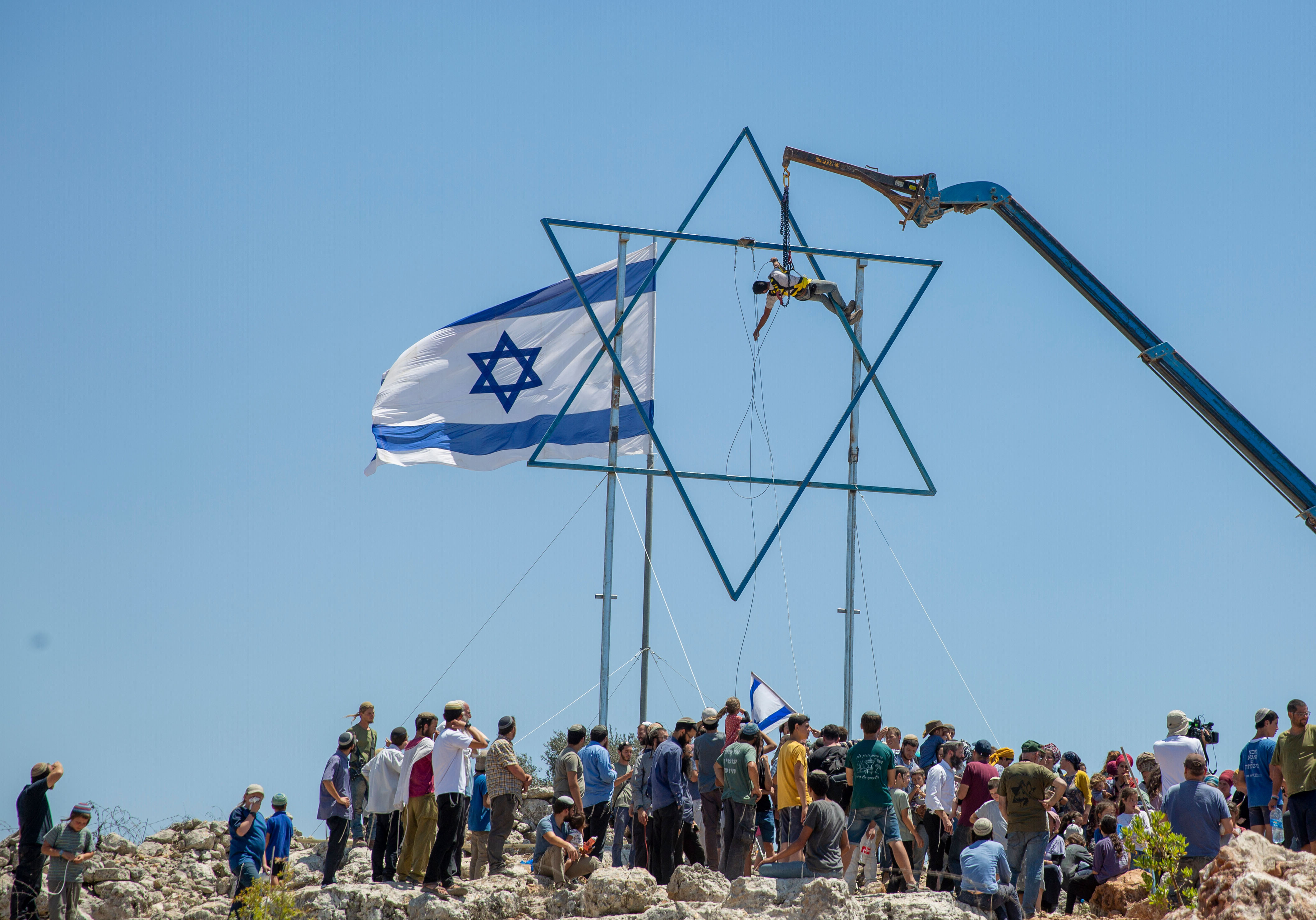 An Israeli settler adjusts a large Star of David in the recently established wildcat outpost of Eviatar near the West Bank city of Nablus, Friday, July 2, 2021. [Ariel Schalit/AP Photo]