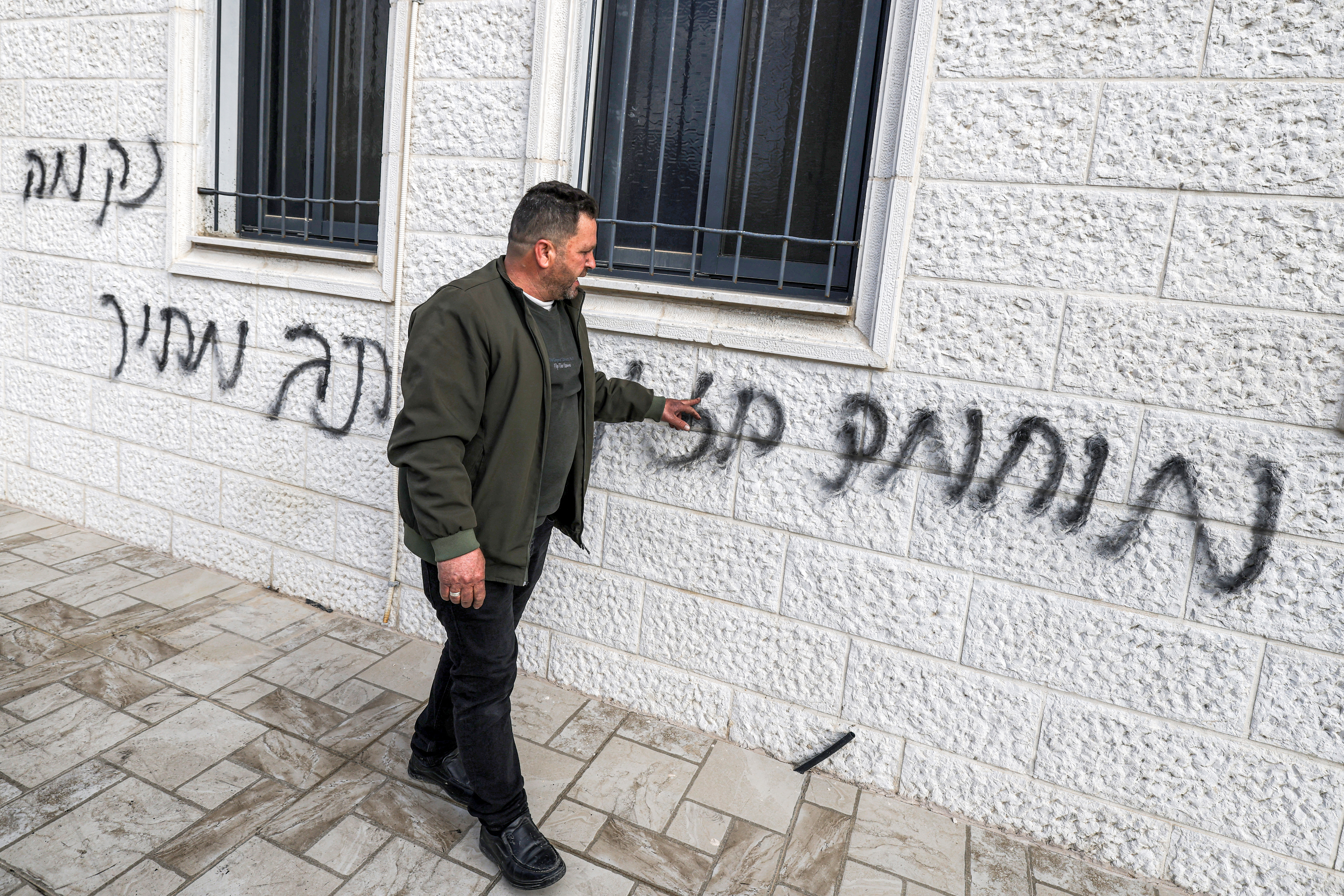 A man inspects offensive Hebrew graffiti on the walls outside the Abu Bakr al-Siddiq Mosque in the village of Tell, west of Nablus in the occupied West Bank, on February 23, 2026 following a reported attack by Israeli settlers.