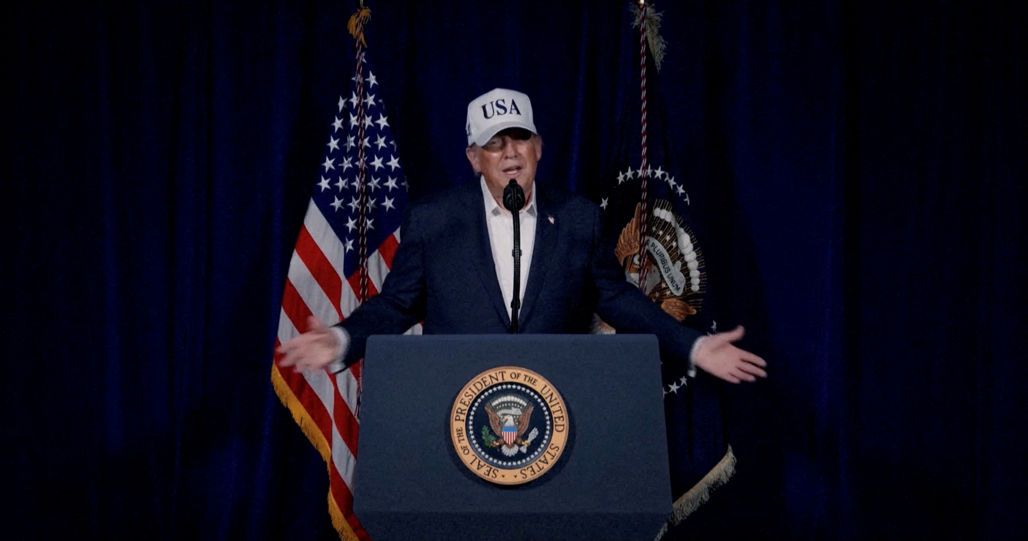 Donald Trump with a USA baseball hat on standing in front of a podium