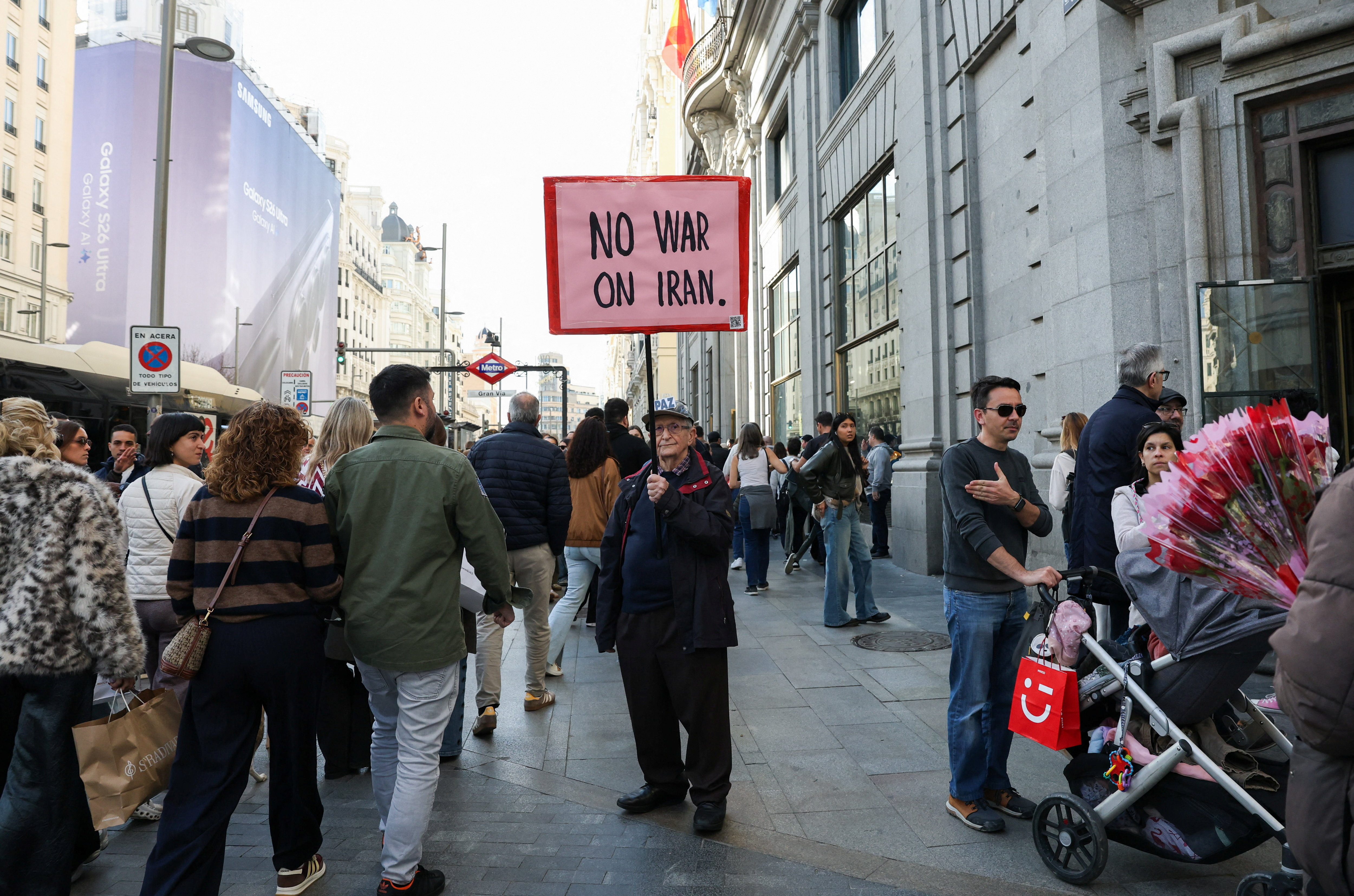 A man on a busy street holds a sign reading 'No war on Iran'.