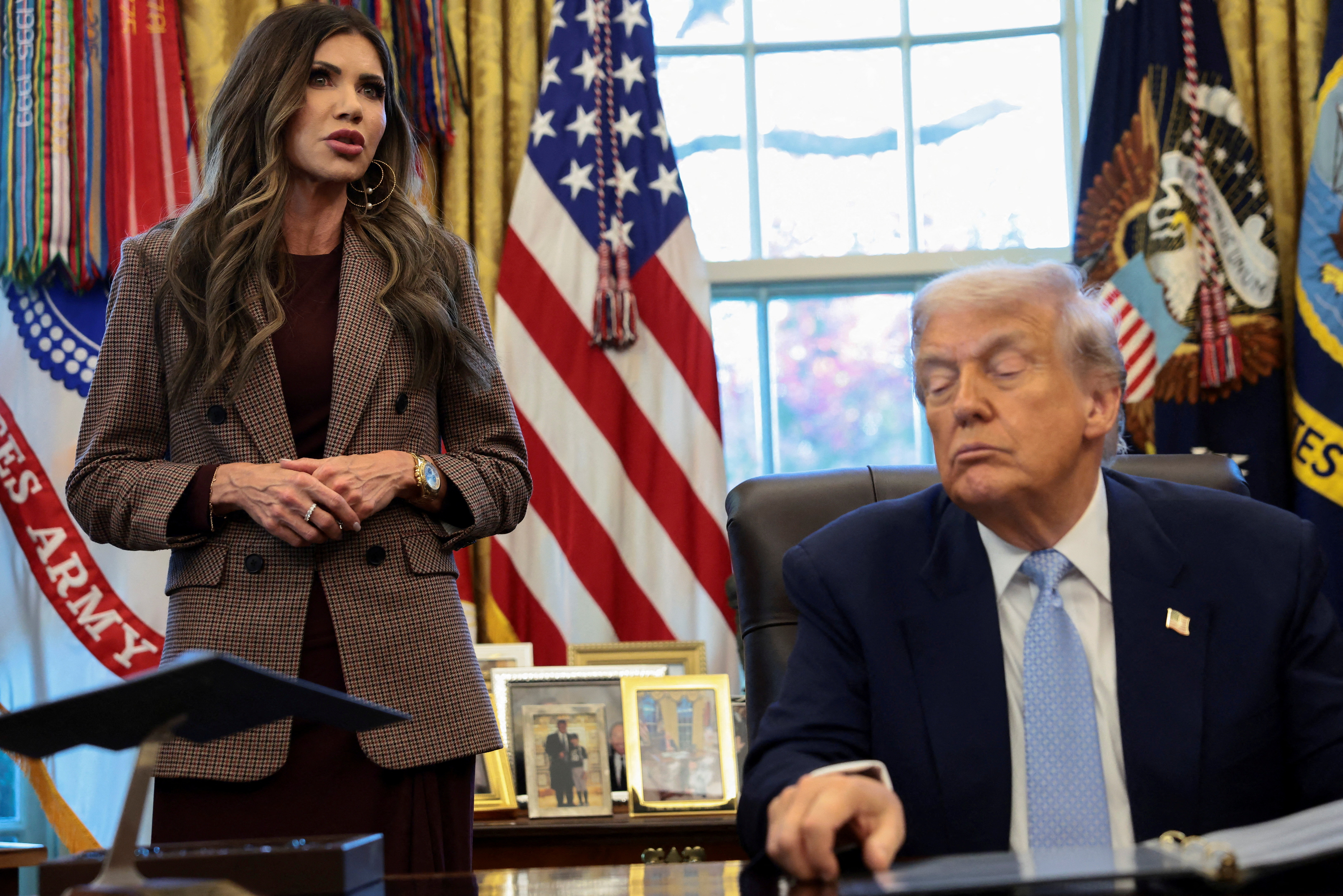 U.S. President Donald Trump sits while U.S. Homeland Security Secretary Kristi Noem stands by his side, as he meets with the White House Task Force on the FIFA World Cup 2026