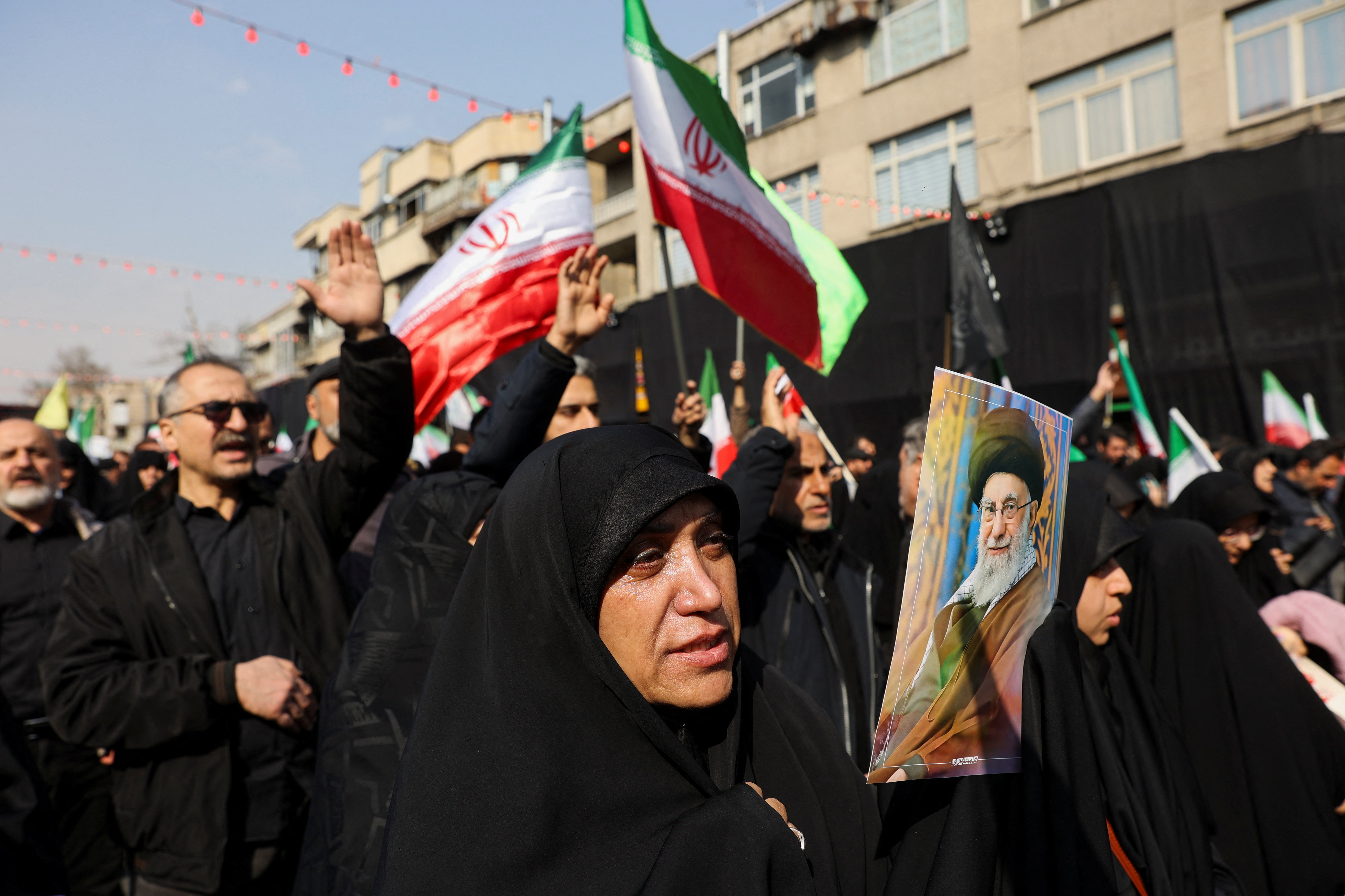 Woman in black with Iranian flags in the background