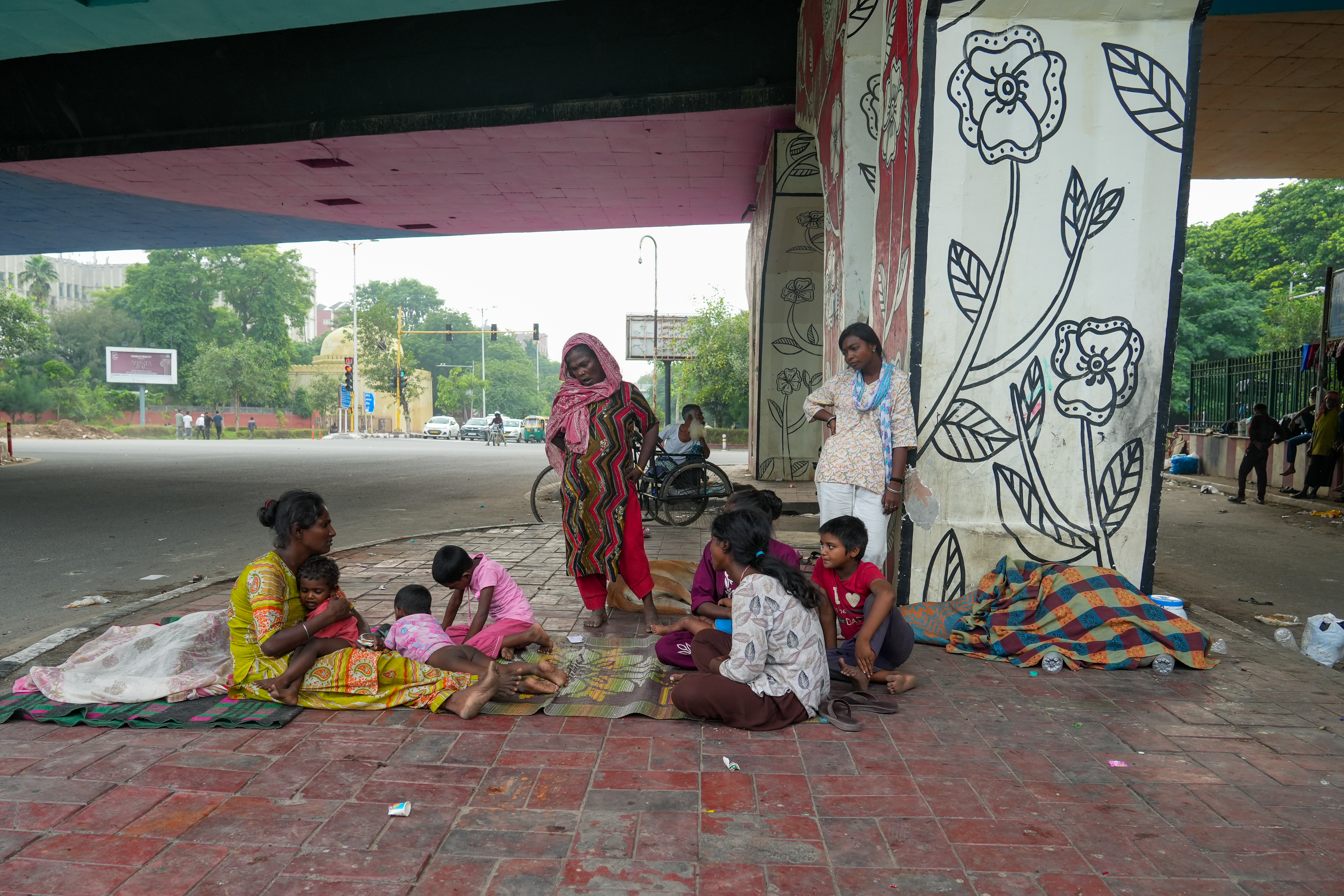 Abida sits with her family and other homeless residents along a busy Delhi street.Thousands of families in the capital live without shelter, exposed to heat, dust, and traffic.Mothers like Abida face the greatest risks, protecting their children amid hunger, illness, and insecurity. [Mubashir Naik/Al Jazeera]