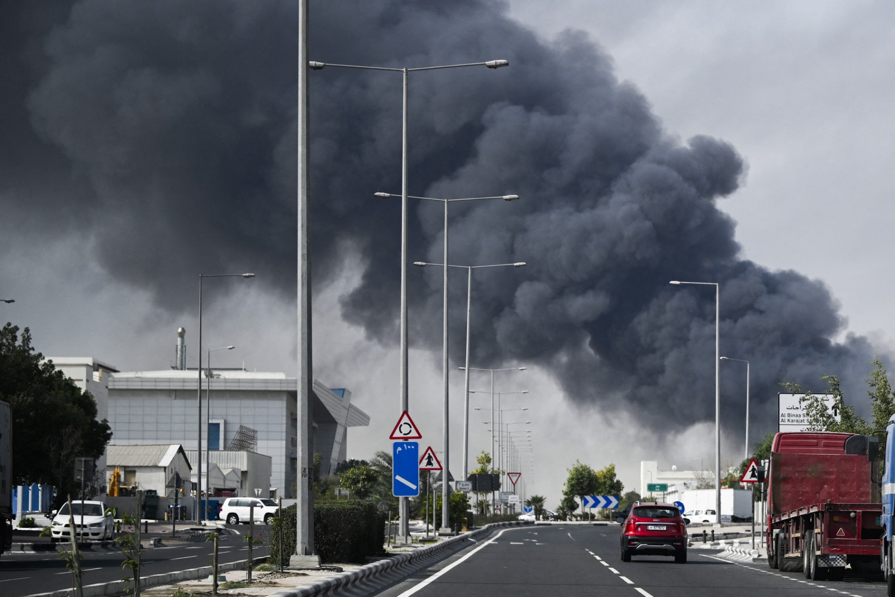 Motorists drive past a plume of smoke.