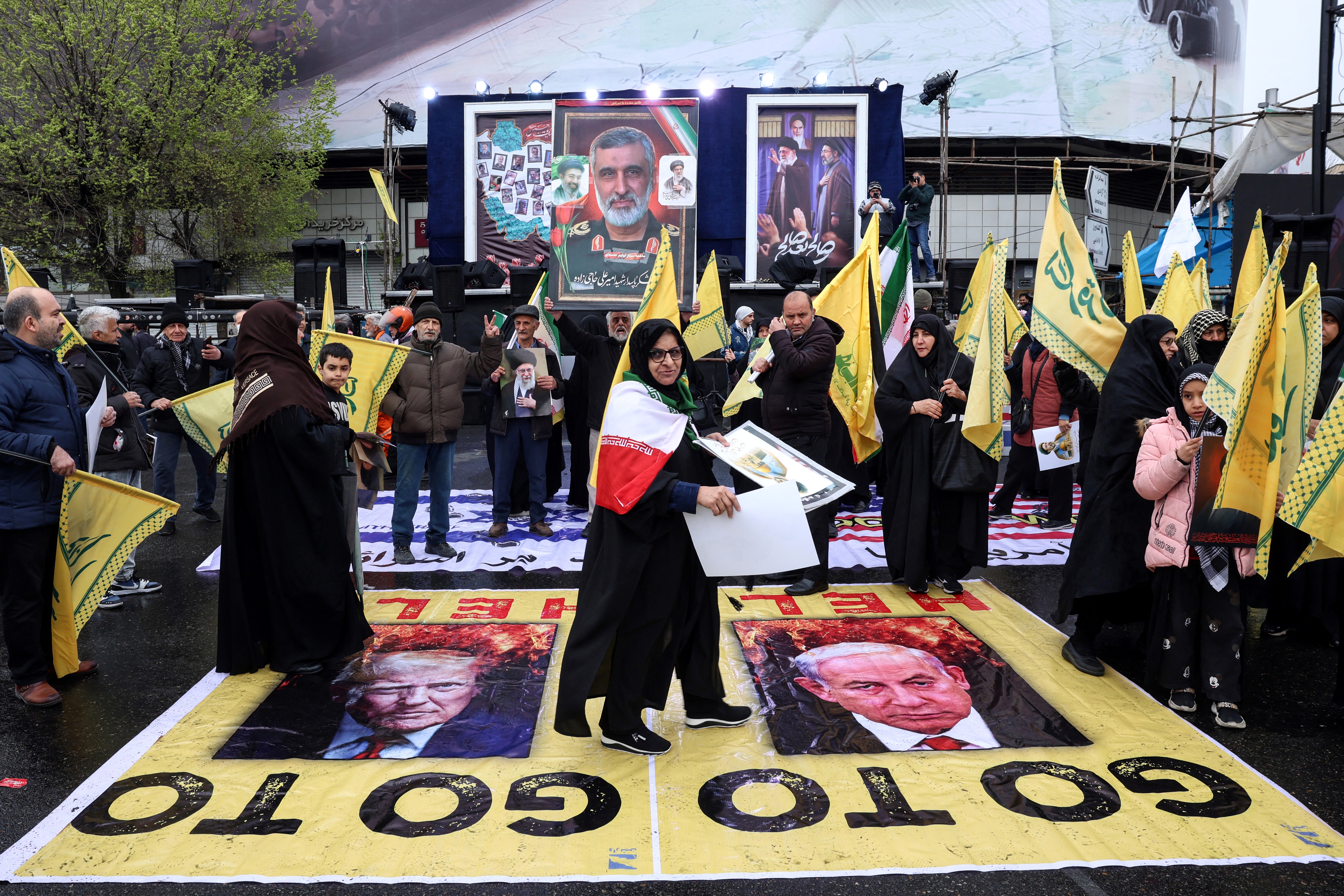 An Iranian woman walks across posters depicting images of US President Donald Trump (L) and Israeli Prime Minister Benjamin Netanyahu as she takes part in a rally.