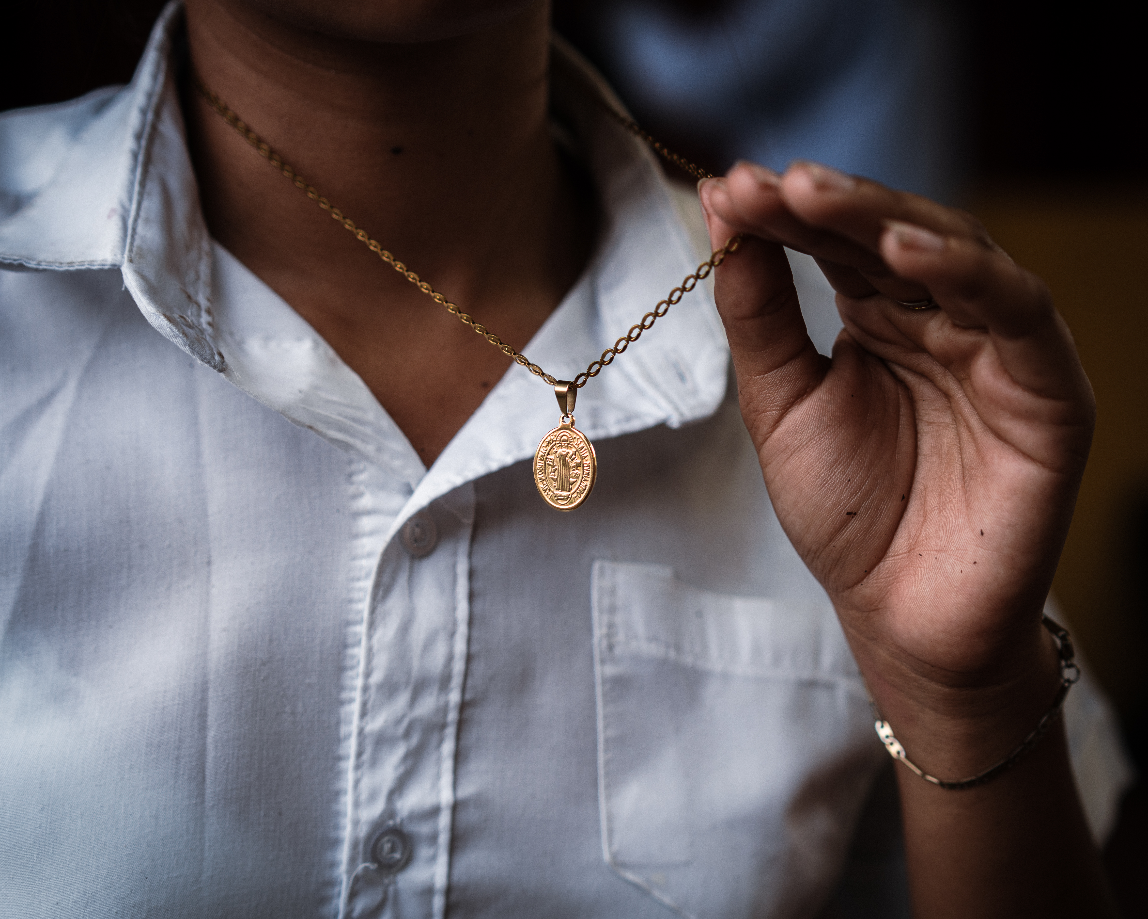 Sara de Perez’s granddaughter, 16, holding the Saint Benedict medallion which her grandmother gifted to her; her father used to wear a similar one. [Euan Wallace/ Al Jazeera]