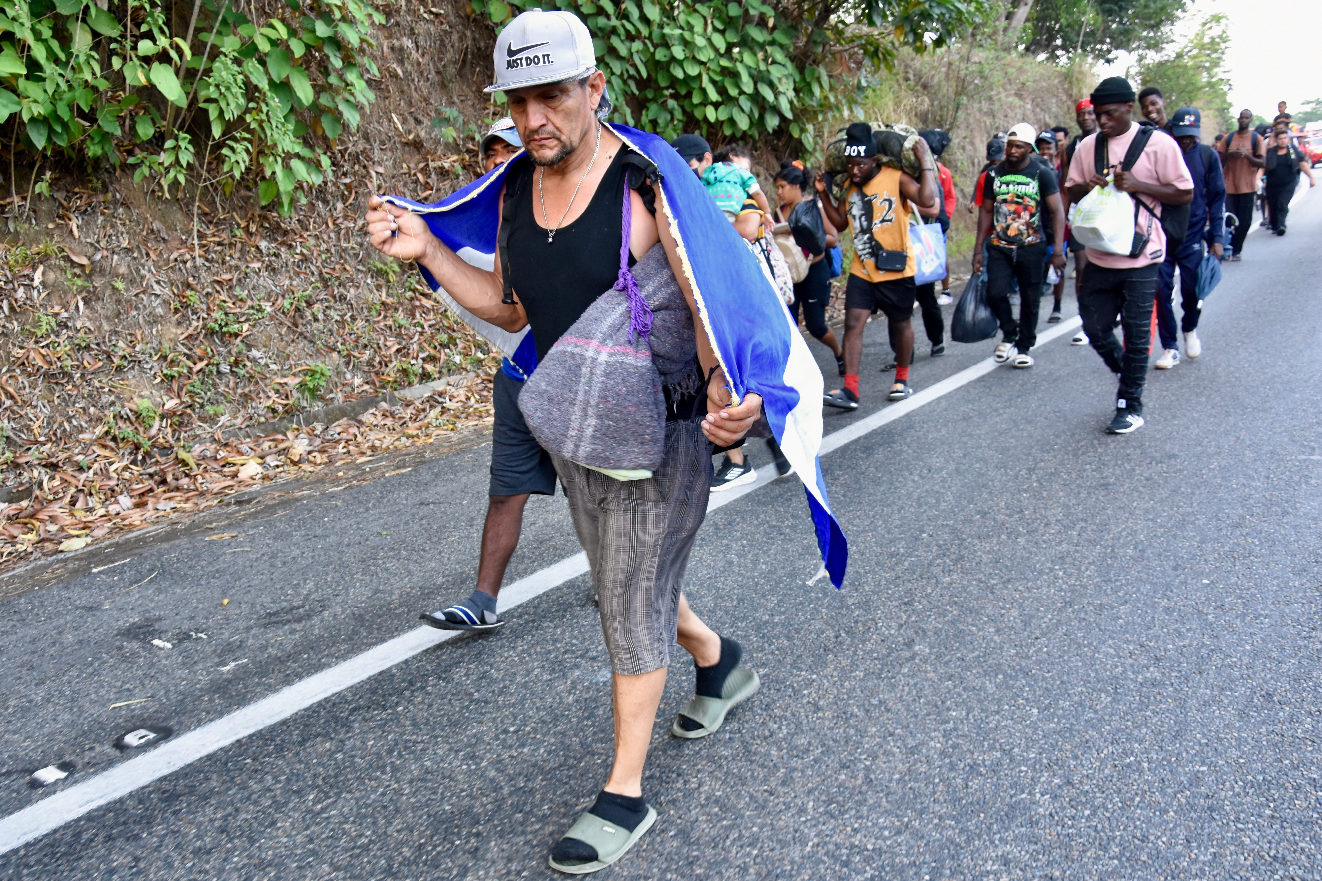 A migrant wearing an El Salvador flag walks on the highway through the municipality of Huehuetan, Chiapas state, Mexico, Wednesday morning, March 25, 2026, with a group of migrants that left Tapachula the previous night. (AP Photo/Edgar H. Clemente)